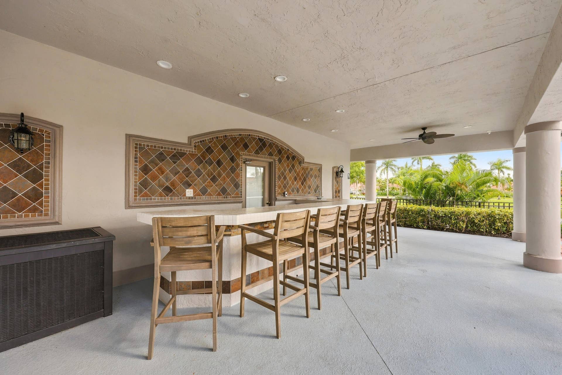 10671 St Thomas Drive, Boca Raton, FL 33498 An inviting covered outdoor entertaining area featuring bar-style seating and ceiling fans, perfect for socializing and enjoying the beautiful South Florida weather.