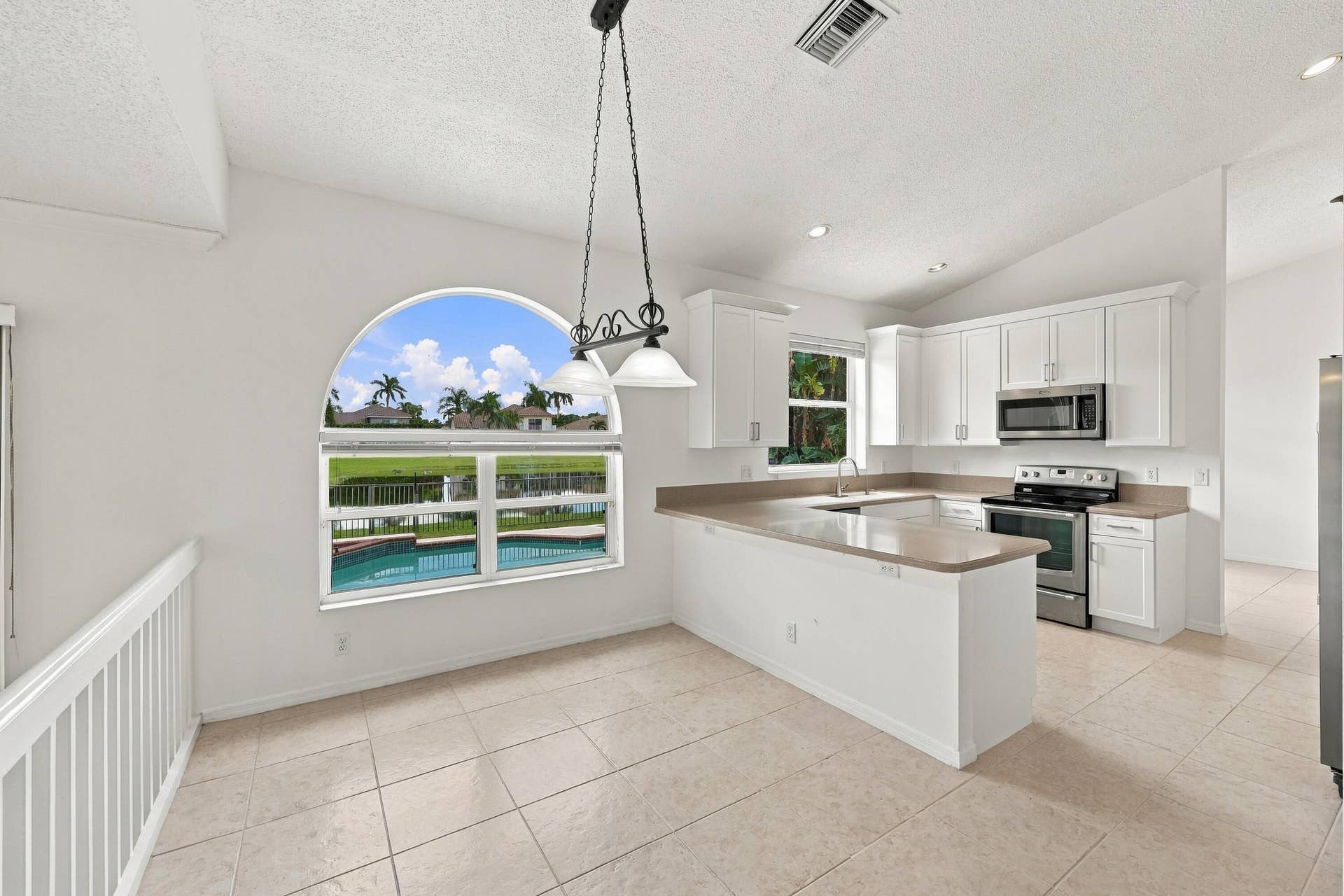 10671 St Thomas Drive, Boca Raton, FL 33498 Enjoy picturesque views of the surrounding greenery from the charming breakfast nook, complete with an oversized arched window, vaulted ceilings, and decorative lighting.