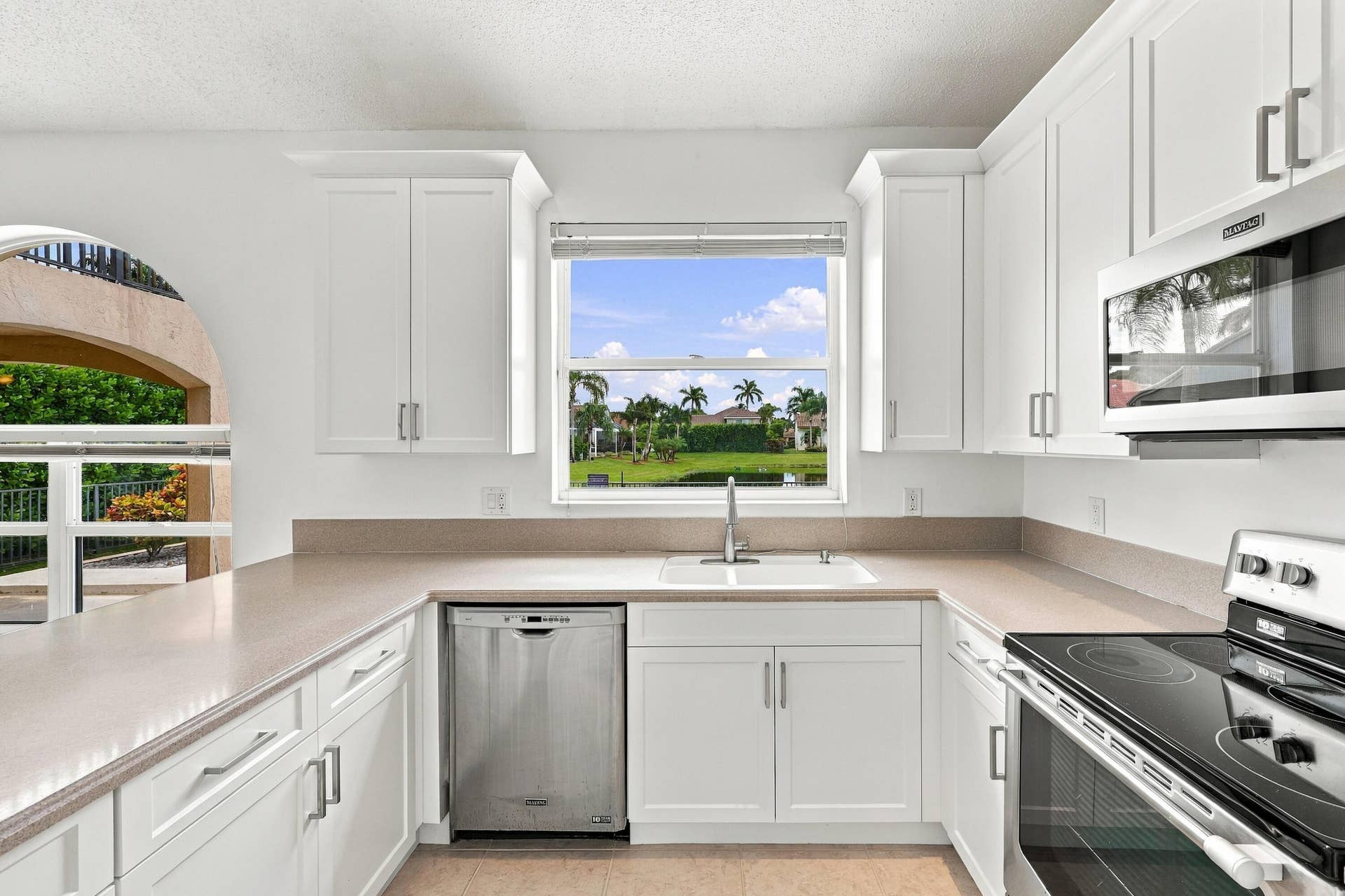 10671 St Thomas Drive, Boca Raton, FL 33498 White cabinetry, stainless steel appliances, and generous counter space complement a large kitchen window overlooking the beautifully landscaped outdoor surroundings.