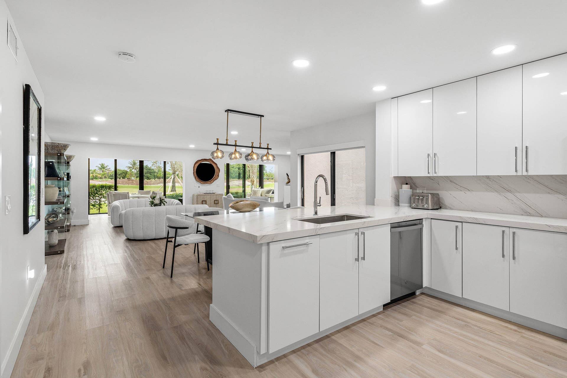 Kitchen featuring white flat-panel cabinetry, light stone-finish countertops, stainless steel undermount sink with arched faucet, recessed lighting, and wood-finish flooring