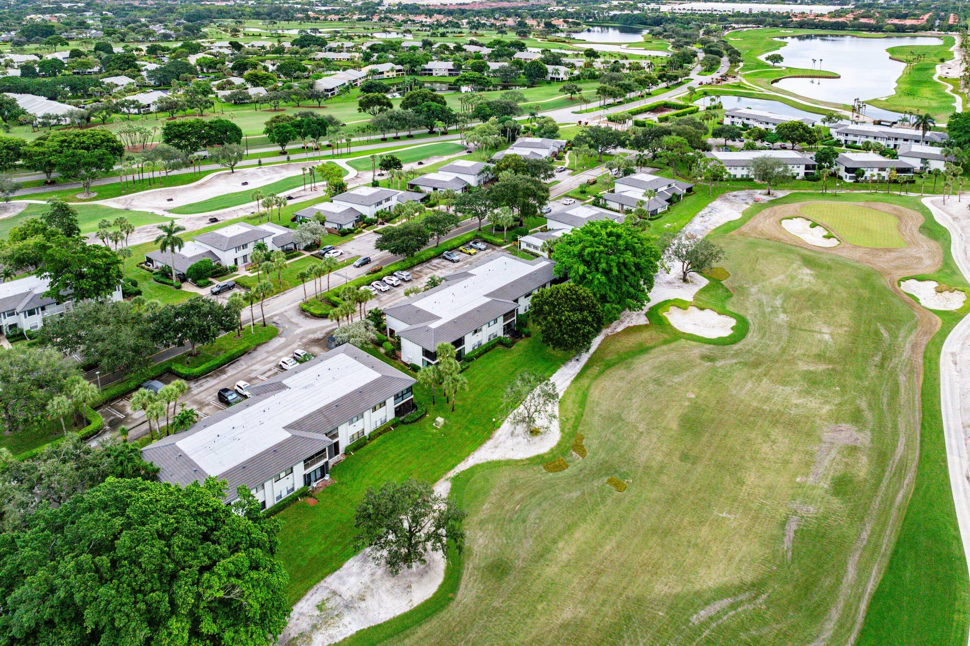 Aerial perspective of multi-family residential structures featuring direct golf course frontage, manicured green space, sand bunkers, and mature landscaping
