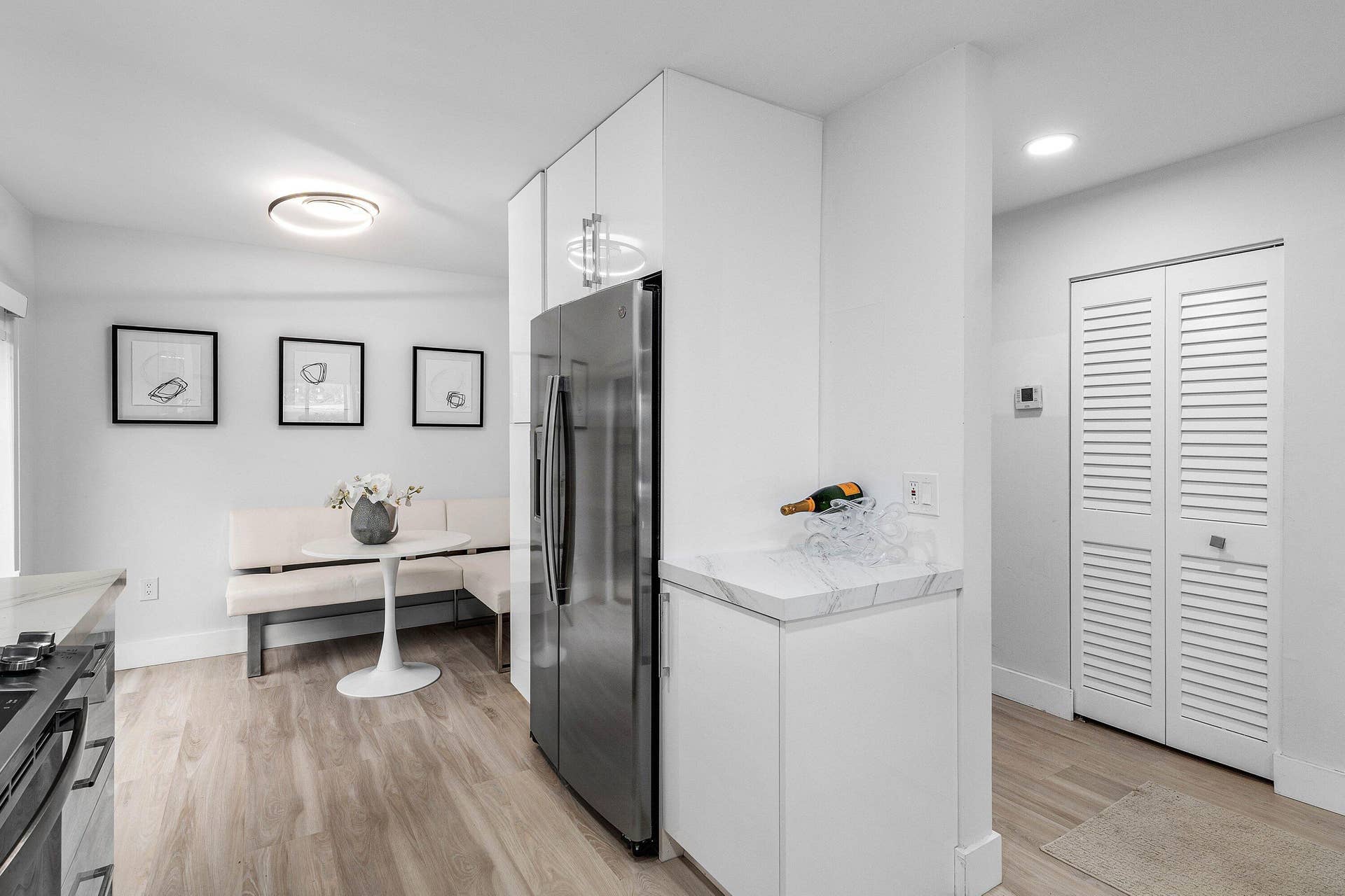 Modern kitchen featuring white flat-panel cabinetry, stainless steel refrigerator, stone-finish countertops, wood-finish flooring, and white louvered closet doors