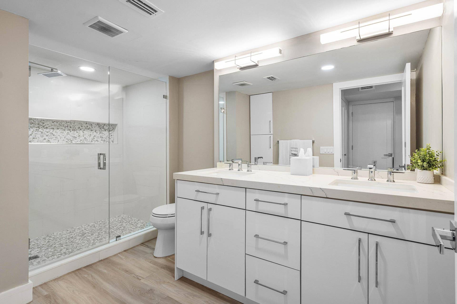 Bathroom featuring a dual-sink vanity with a solid surface countertop, glass-enclosed shower with tiled flooring and built-in shelving, white cabinetry, and wood-finish flooring