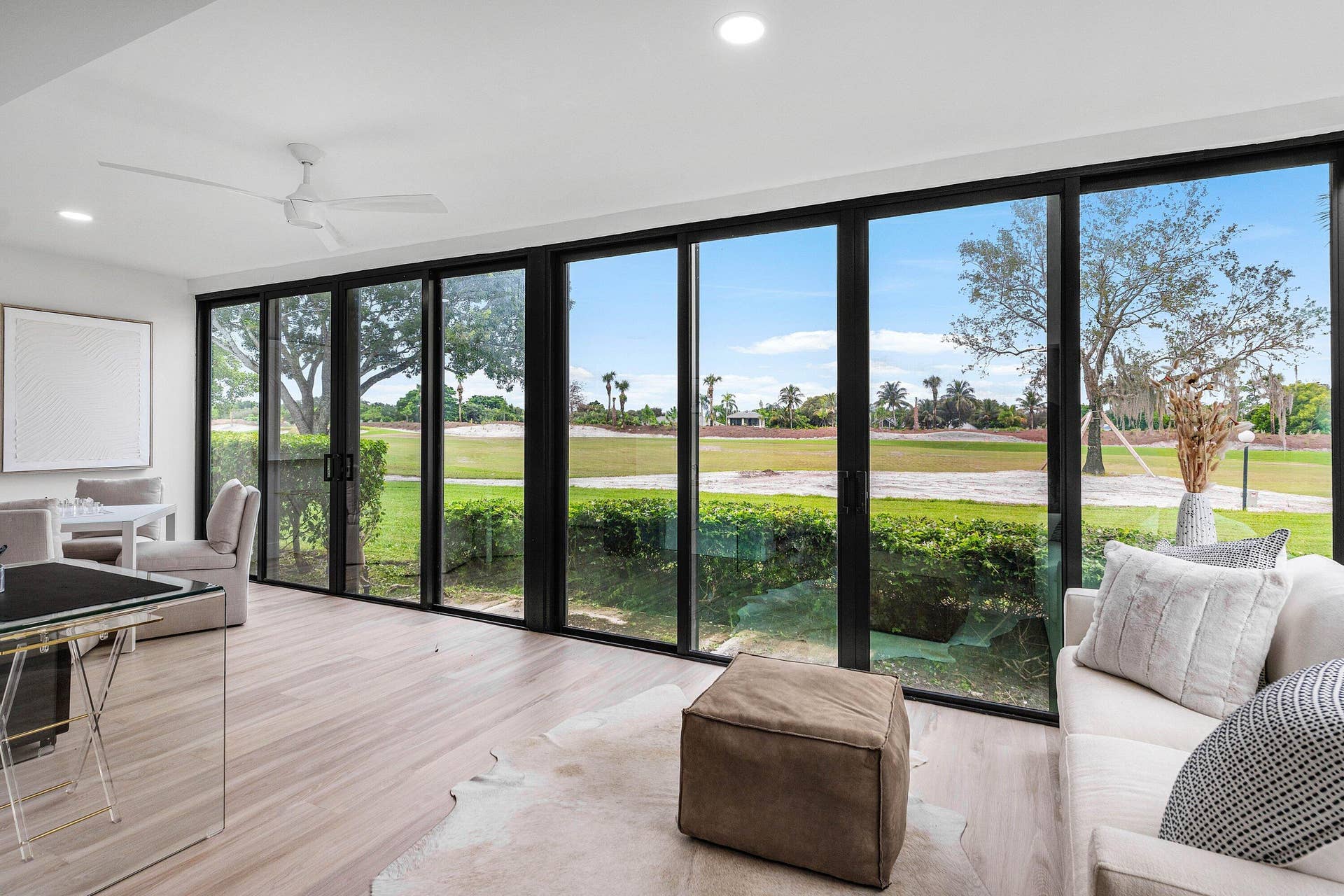 Floor-to-ceiling black-framed sliding glass doors, wood-finish flooring, recessed lighting, and a white ceiling fan