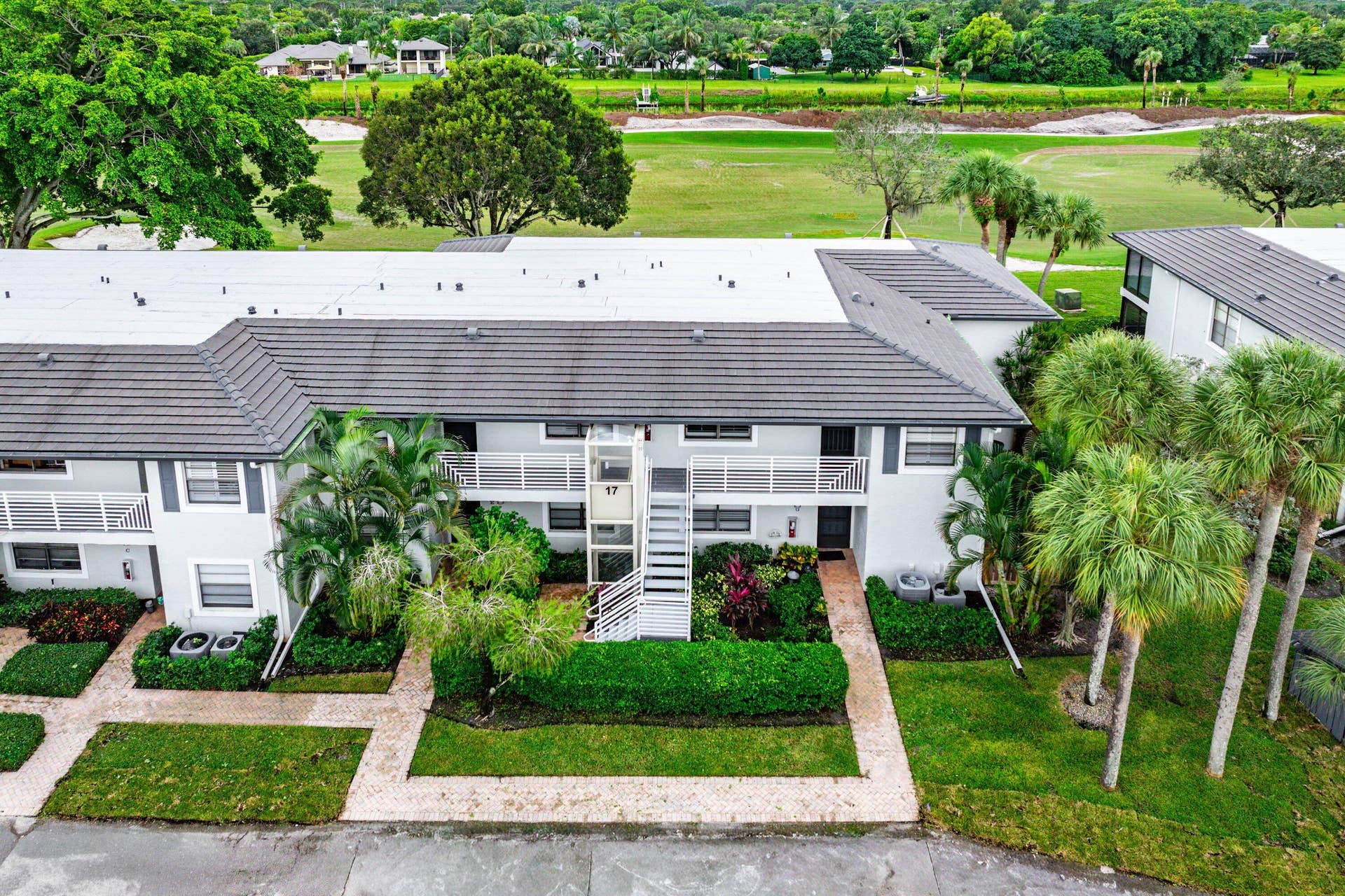 Multi-story exterior featuring a tile roof, paved walkways, mature landscaping, and an integrated stairwell