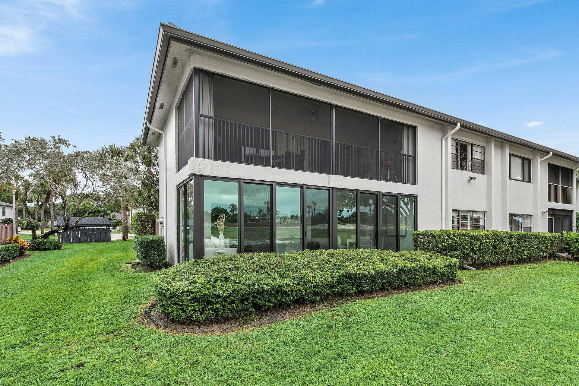 Two-story exterior featuring light-colored stucco finish, screened balcony with dark-toned metal railing, and floor-to-ceiling glass panel windows