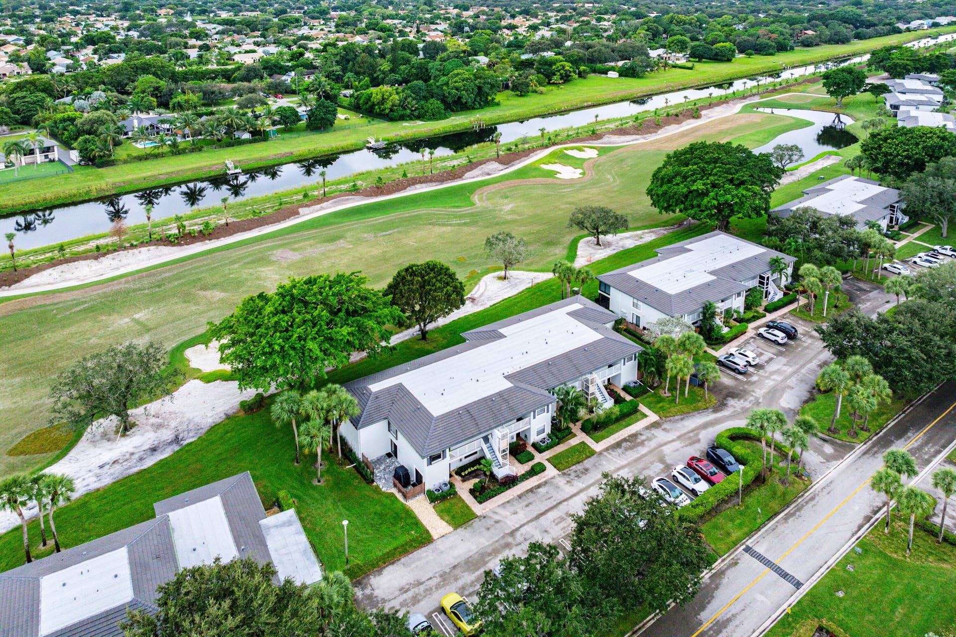 Aerial perspective featuring multi-unit structures with shingled roofing, paved surface parking, manicured landscaping, and canal frontage