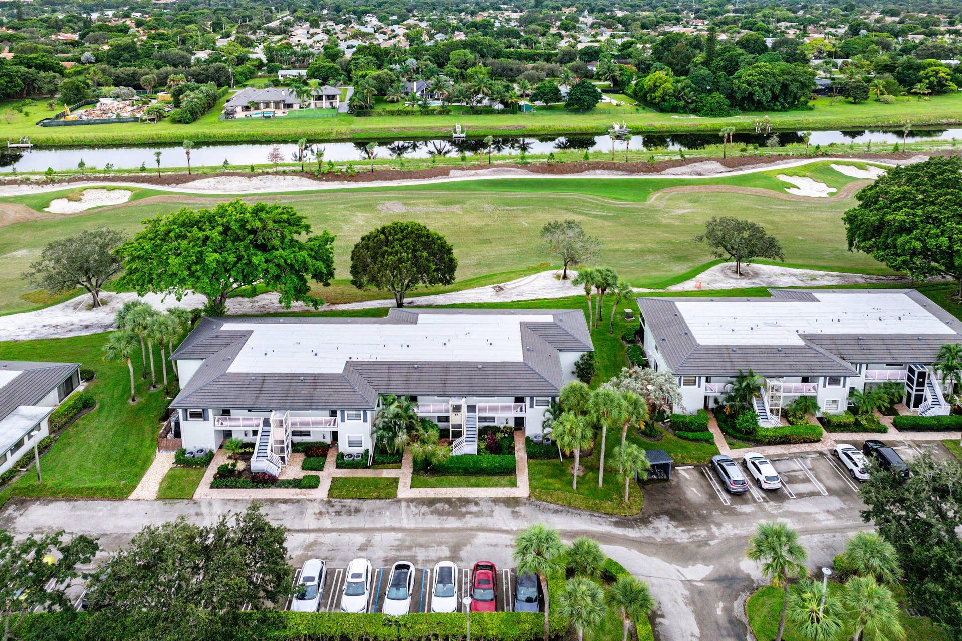 Aerial perspective featuring multi-unit structures with shingled roofs, integrated parking lots, and direct exposure to a golf course and waterway