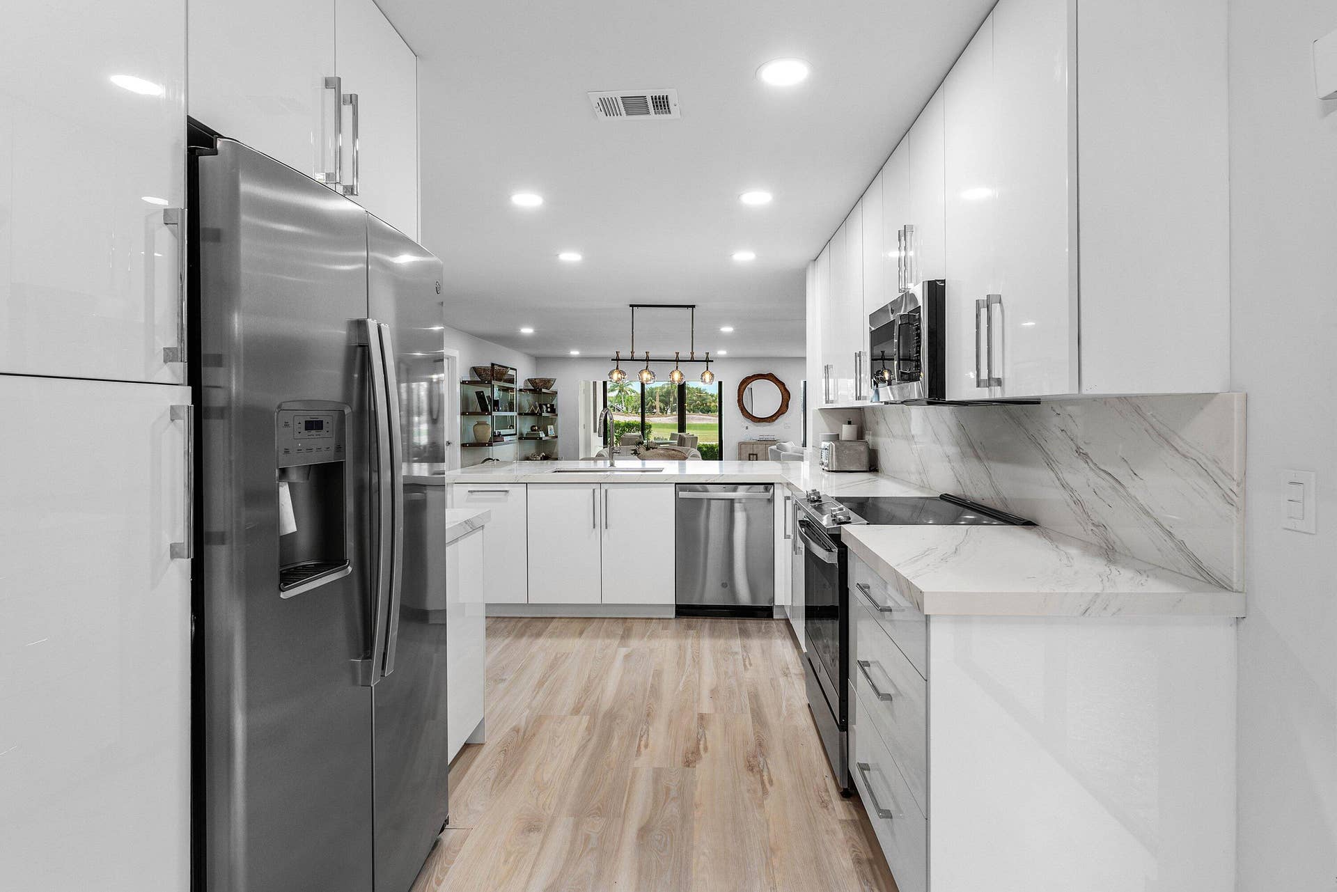 Modern kitchen featuring high-gloss white cabinetry, stainless steel appliances, stone-finish countertops with matching backsplash, and wood-finish flooring