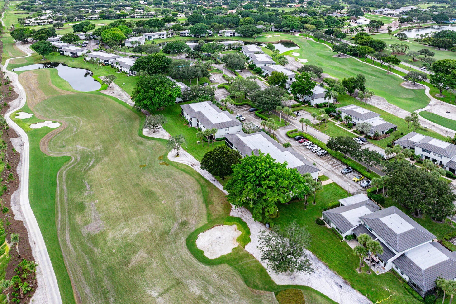 Aerial perspective featuring multi-building residential structures, expansive golf course grounds, integrated water features, and mature landscaping