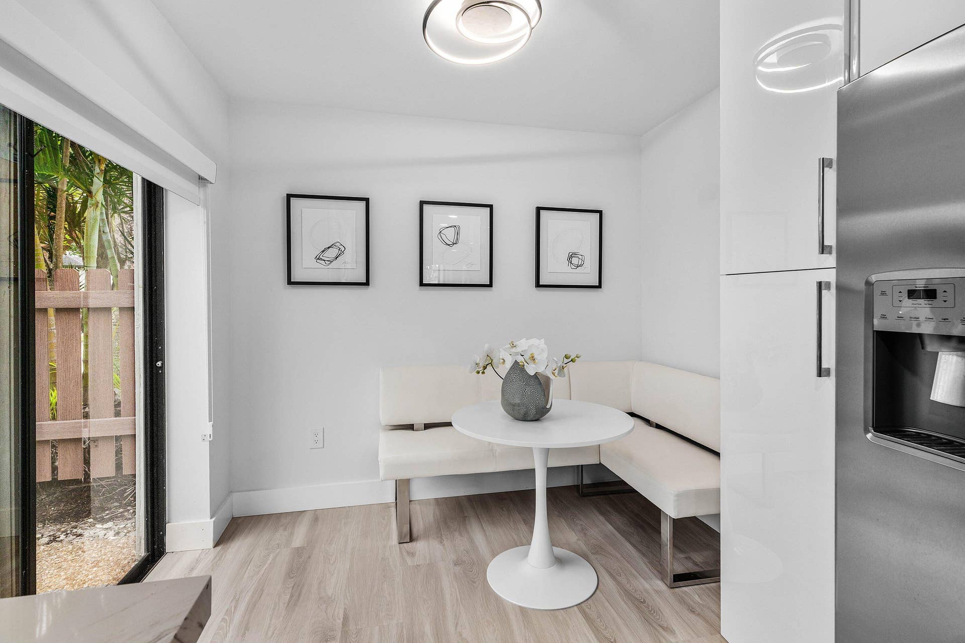 High-gloss cabinetry, stainless steel refrigerator, wood-finish flooring, sliding glass door, and flush-mount circular lighting