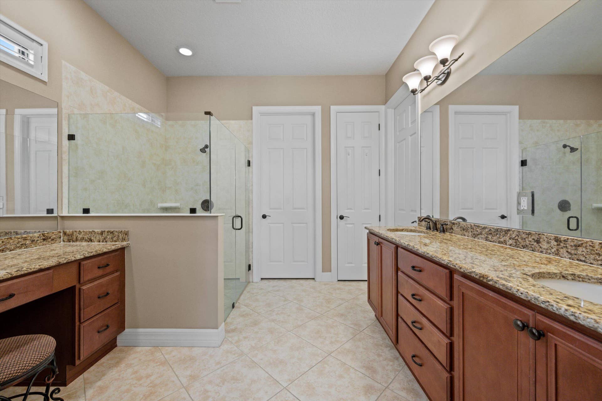 Bathroom featuring dual-sink vanity with stone-finish countertops, glass-enclosed shower, dedicated vanity seating area, and tile flooring