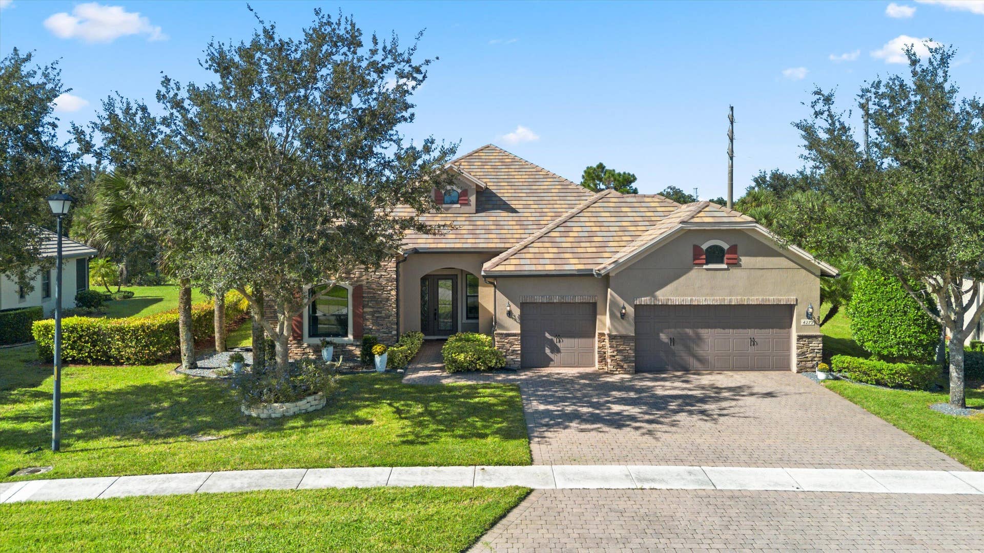 Residence featuring stone accents, a multi-car garage, a paver driveway, and a tiled roof
