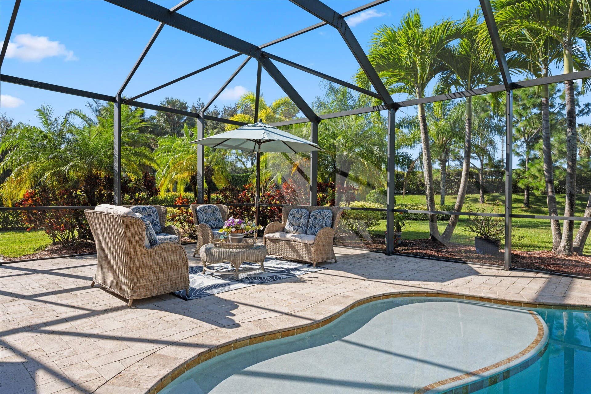 Screen-enclosed patio featuring paver decking, an in-ground pool, and mature palm trees