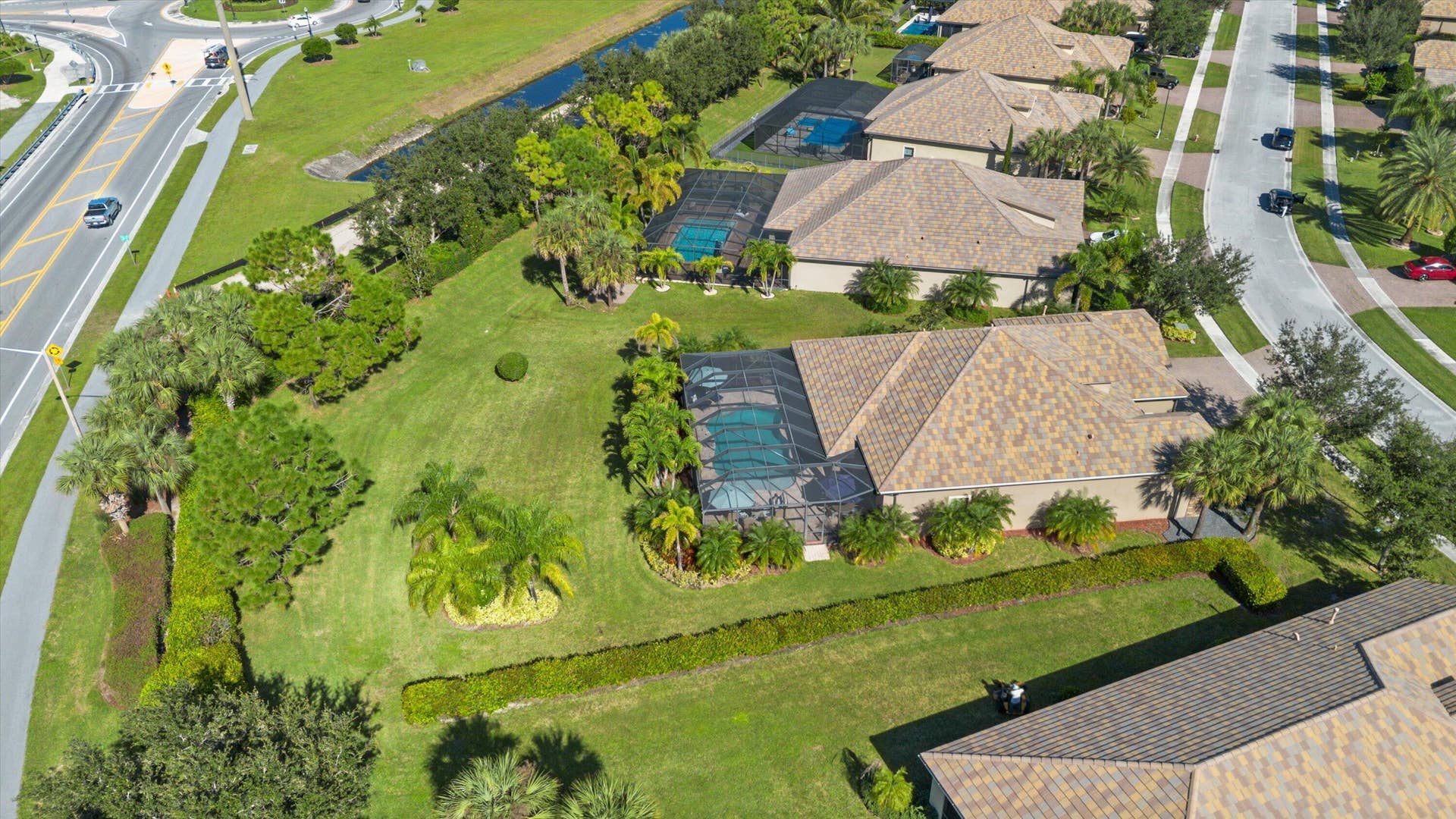 Aerial view of property featuring a screened-in swimming pool, expansive lawn, mature palm trees, and perimeter landscaping
