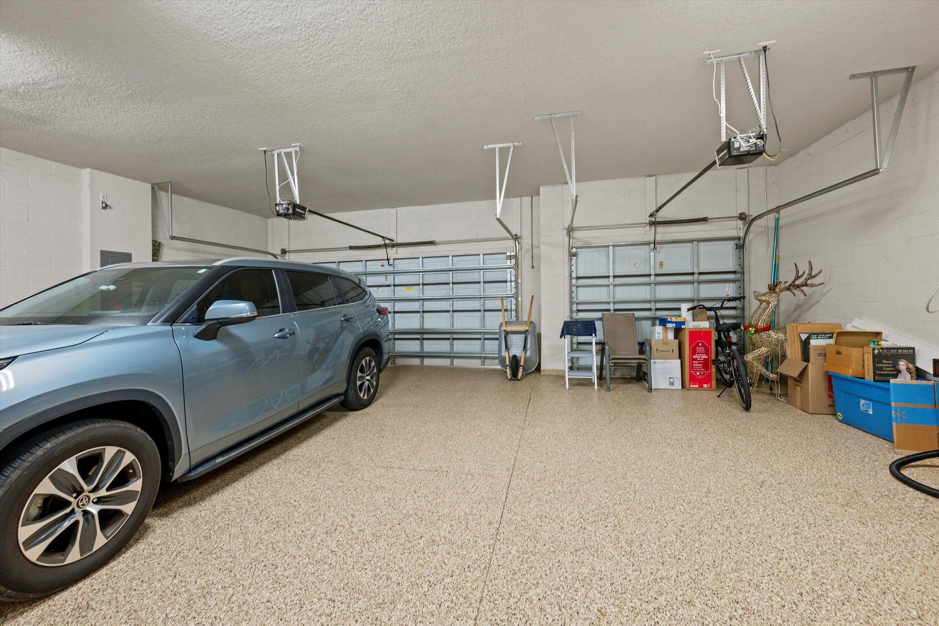 Three-car garage featuring epoxy-coated flooring, two individual metal roll-up doors, and ceiling-mounted automatic door openers