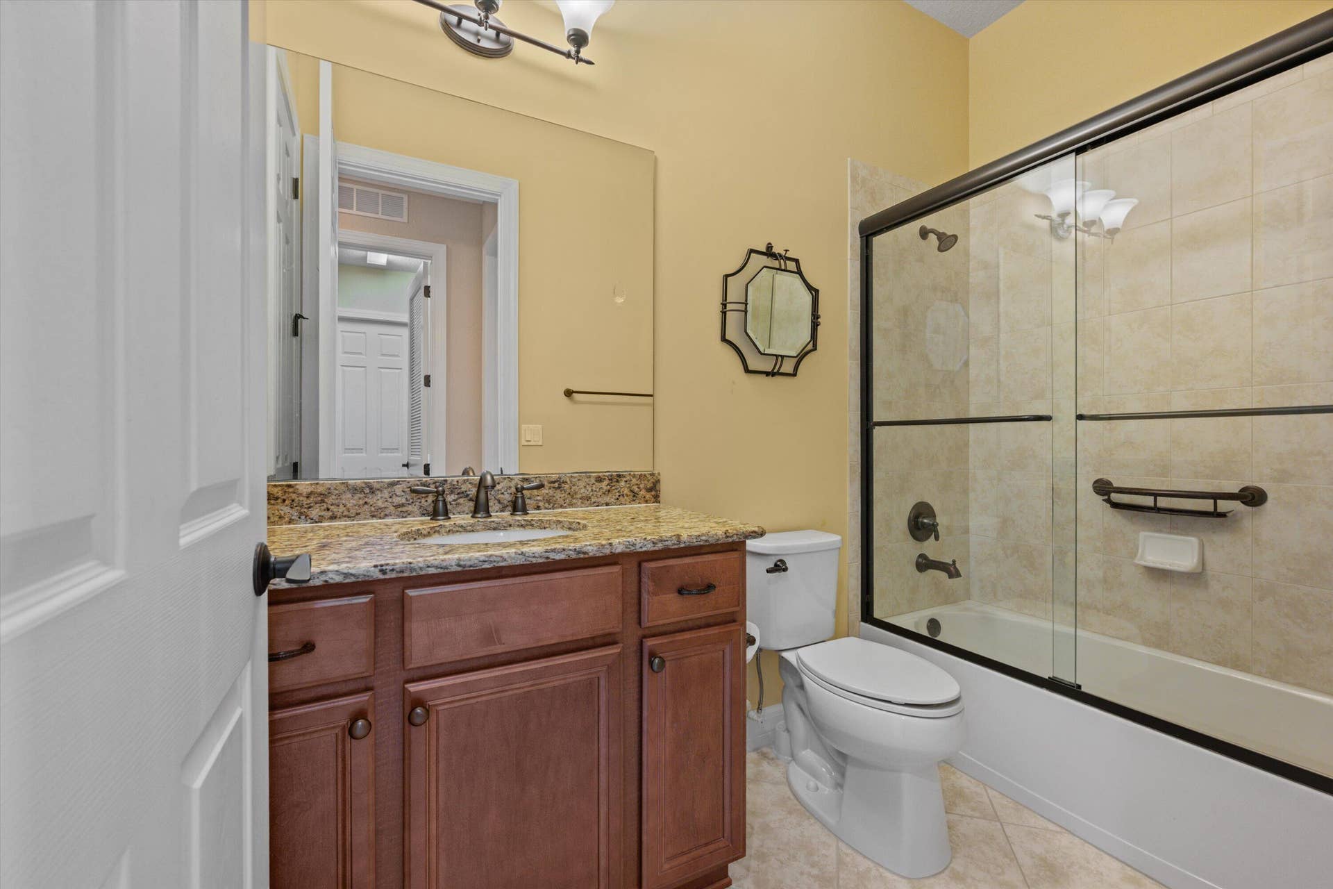 Bathroom featuring a vanity with stone-finish countertop, undermount sink, dark wood cabinetry, and a tub-shower combination enclosed by a framed glass door