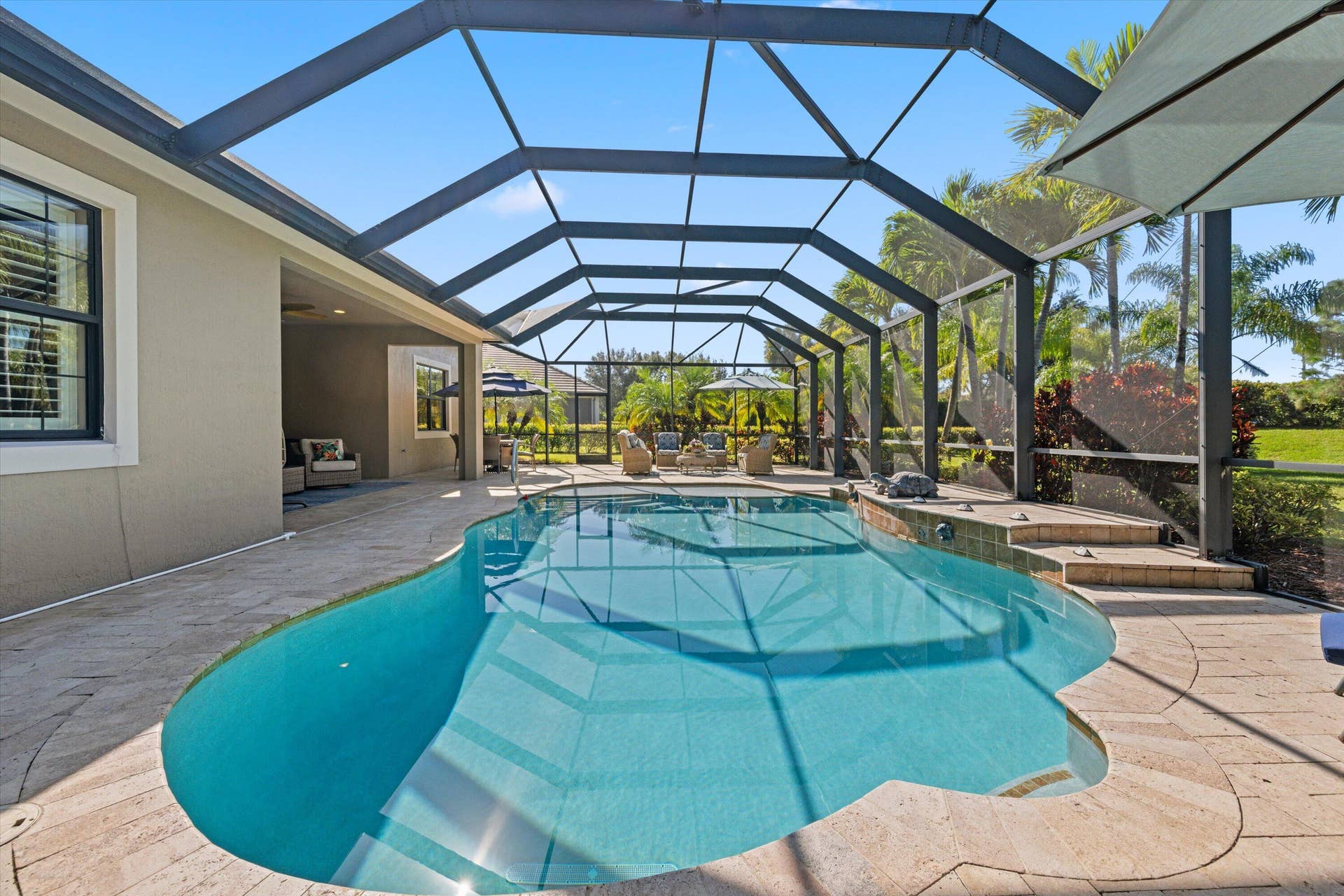 Screened-in patio featuring a custom-shaped salt water pool, raised spillover area, stone-finish decking, and exterior house access