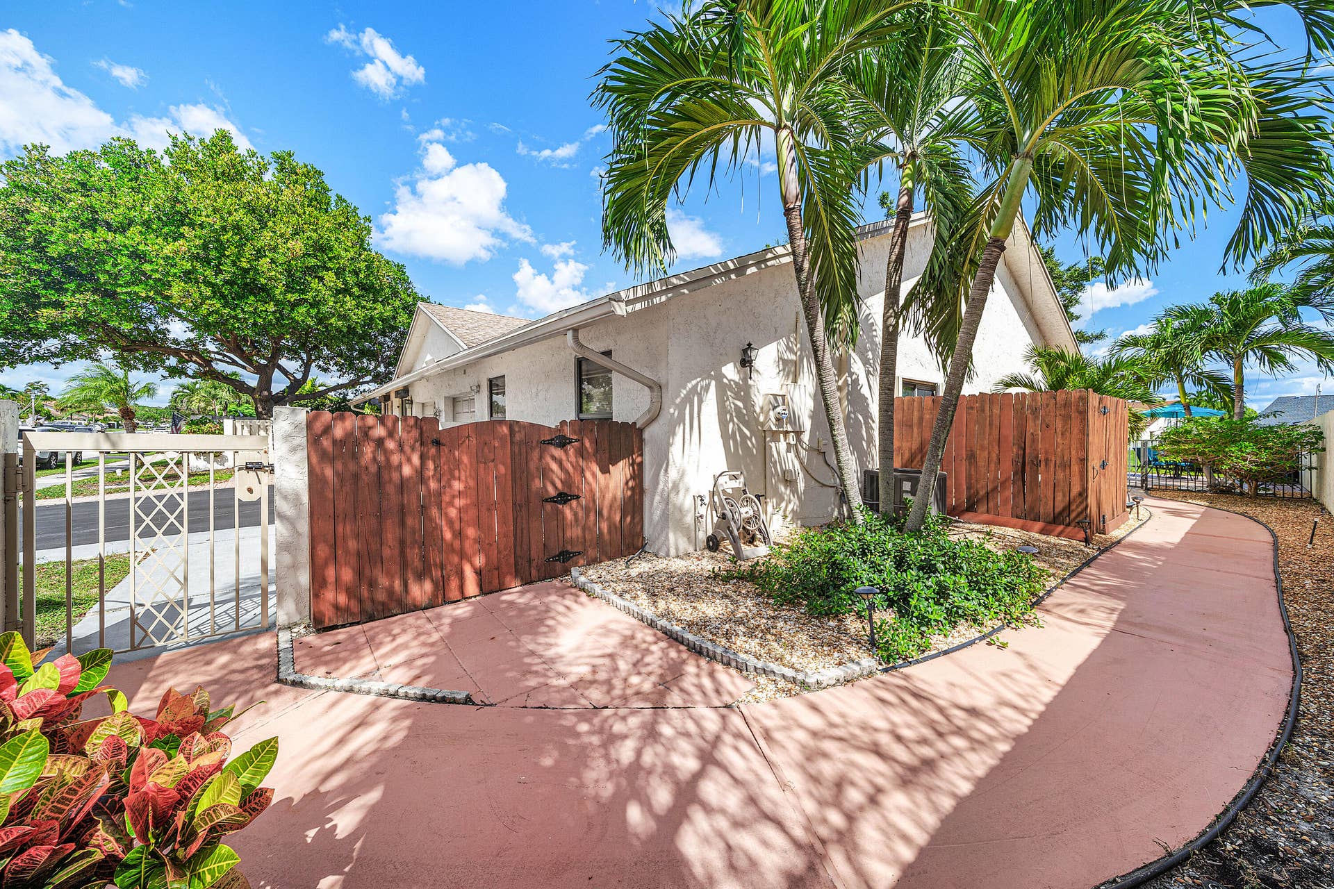 503 SW 29TH Avenue, Delray Beach, FL 33445 Stucco exterior featuring mature palm trees, a wood privacy fence, a decorative lattice metal gate, and a paved walkway