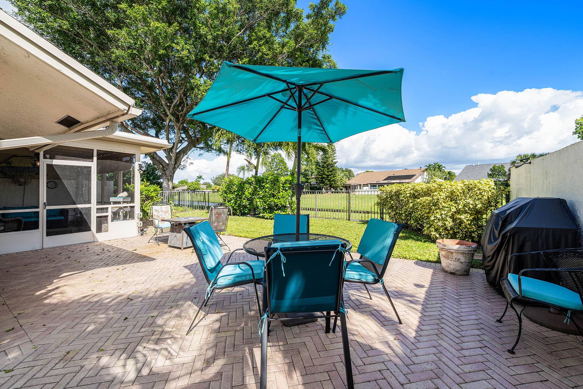 503 SW 29TH Avenue, Delray Beach, FL 33445 Brick paver patio featuring an enclosed screened-in porch, metal perimeter fencing, and mature landscaping