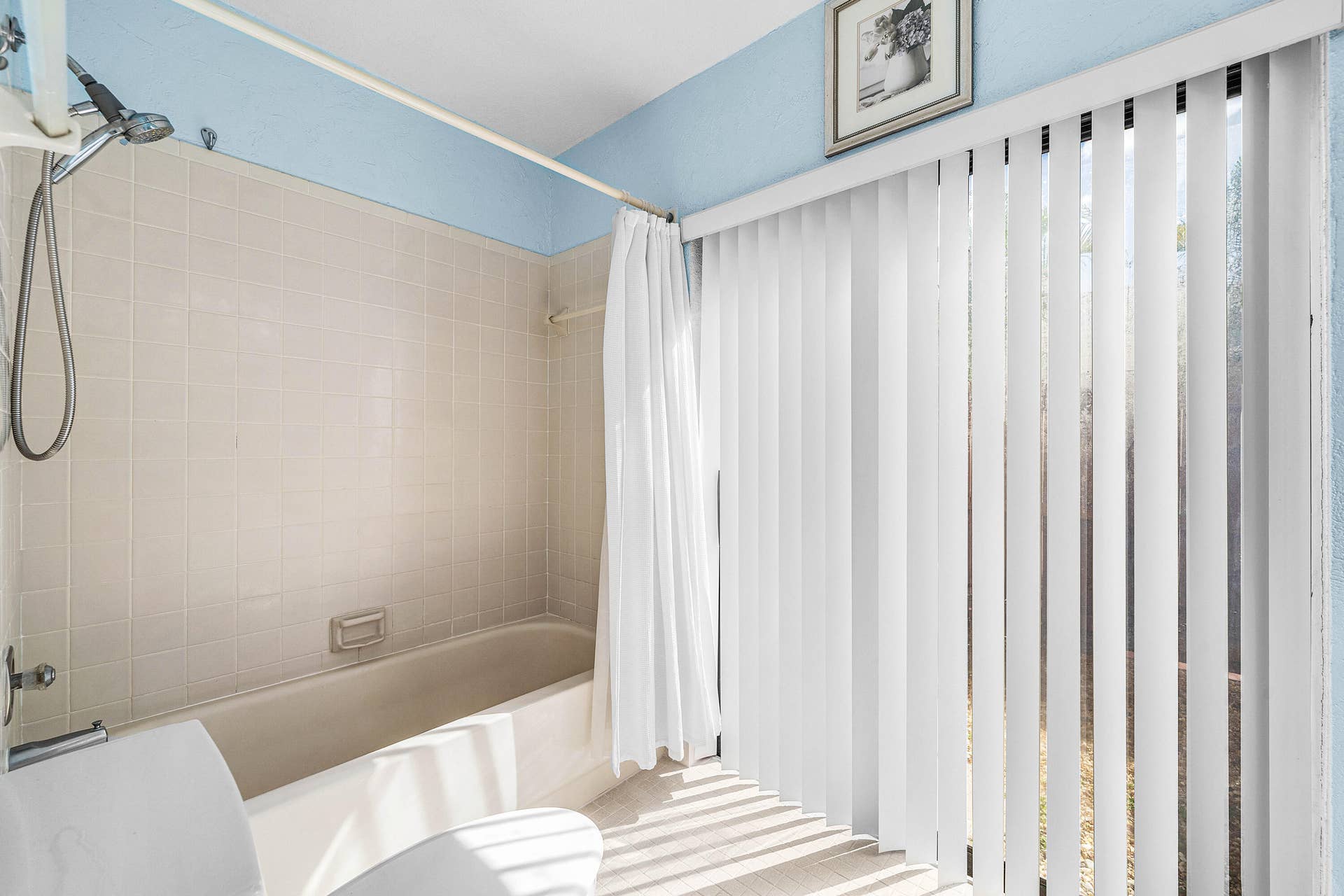 503 SW 29TH Avenue, Delray Beach, FL 33445 Bathtub enclosure with tiled wall surround, wall-mounted hand-held shower fixture, and floor-to-ceiling vertical blinds