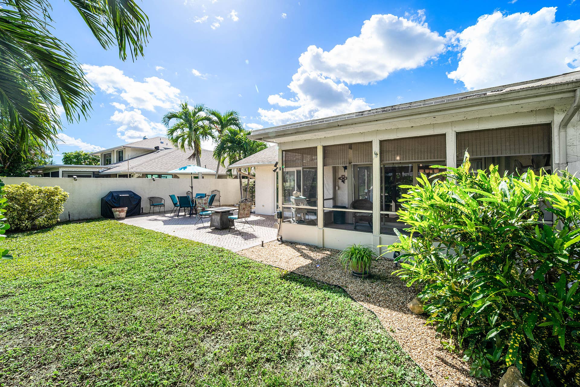 503 SW 29TH Avenue, Delray Beach, FL 33445 Backyard featuring a screened-in lanai, concrete paver patio, stone ground cover, and perimeter privacy wall