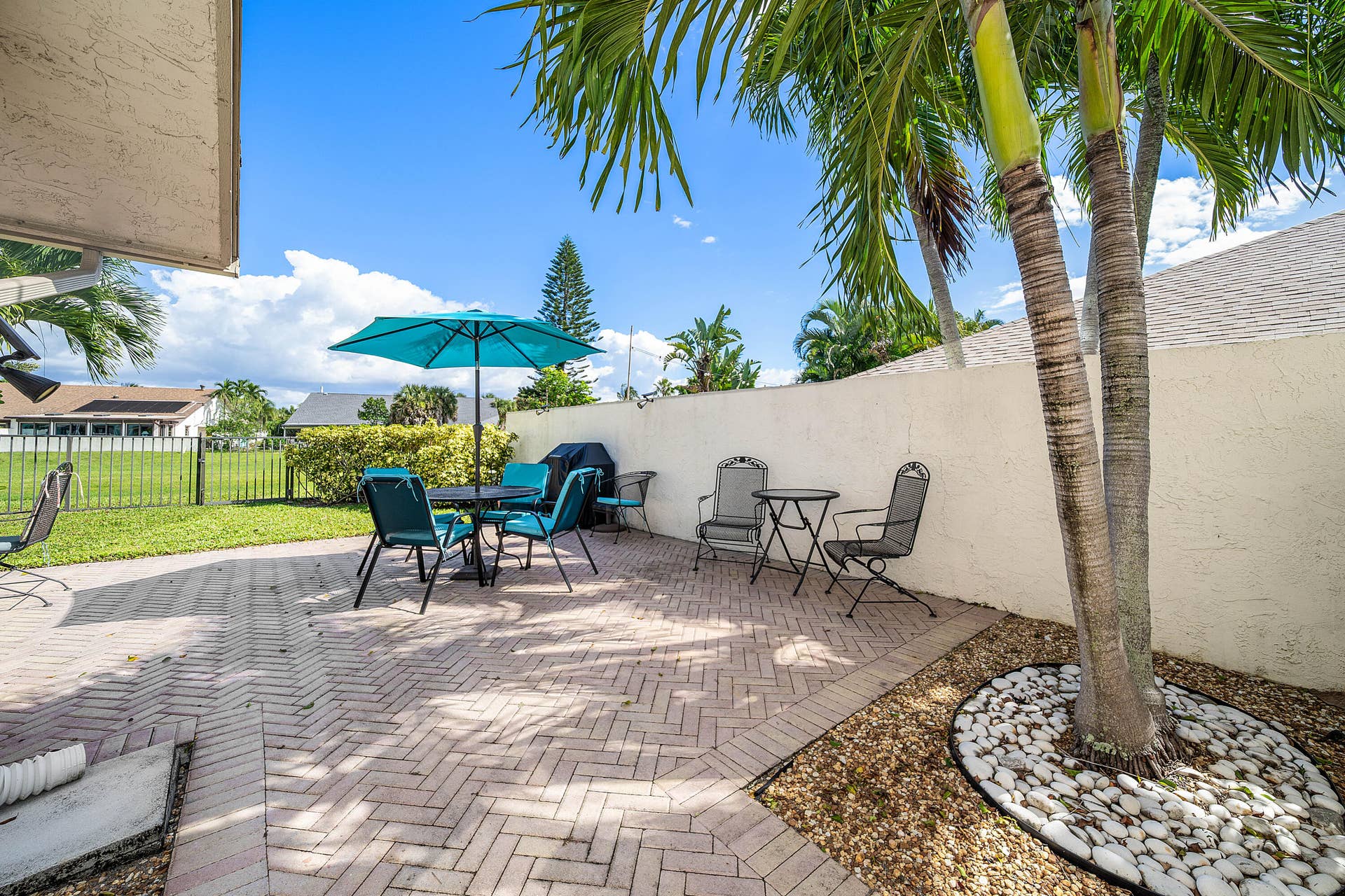 503 SW 29TH Avenue, Delray Beach, FL 33445 Outdoor patio featuring herringbone-patterned brick pavers, a privacy wall, mature palm trees, and decorative stone landscaping