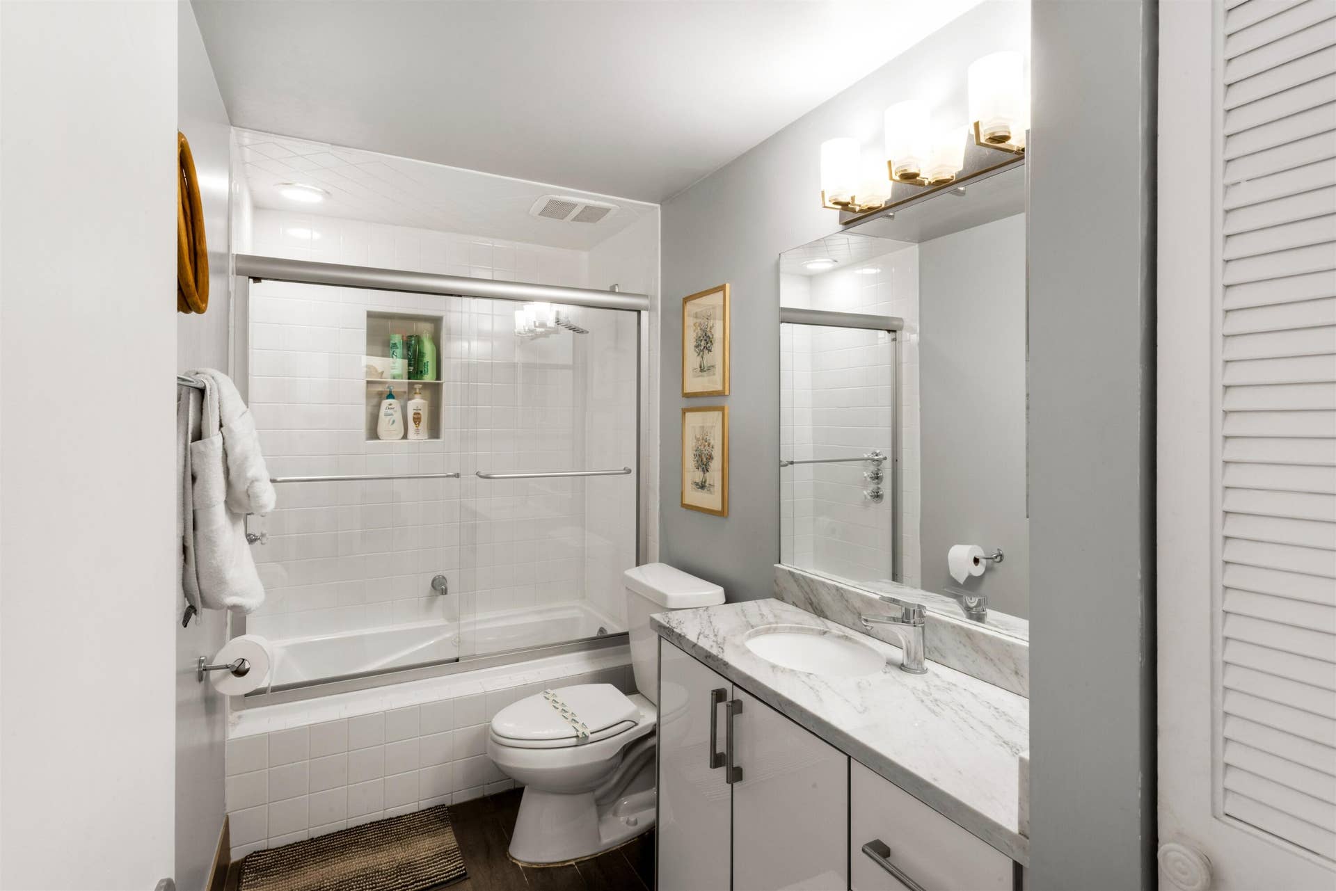 419 E Atlantic Avenue, Delray Beach, FL 33483 Bathroom featuring a vanity with stone-finish countertop, undermount sink, three-light fixture above a mirror, tiled shower enclosure with built-in niche, and wood-finish flooring