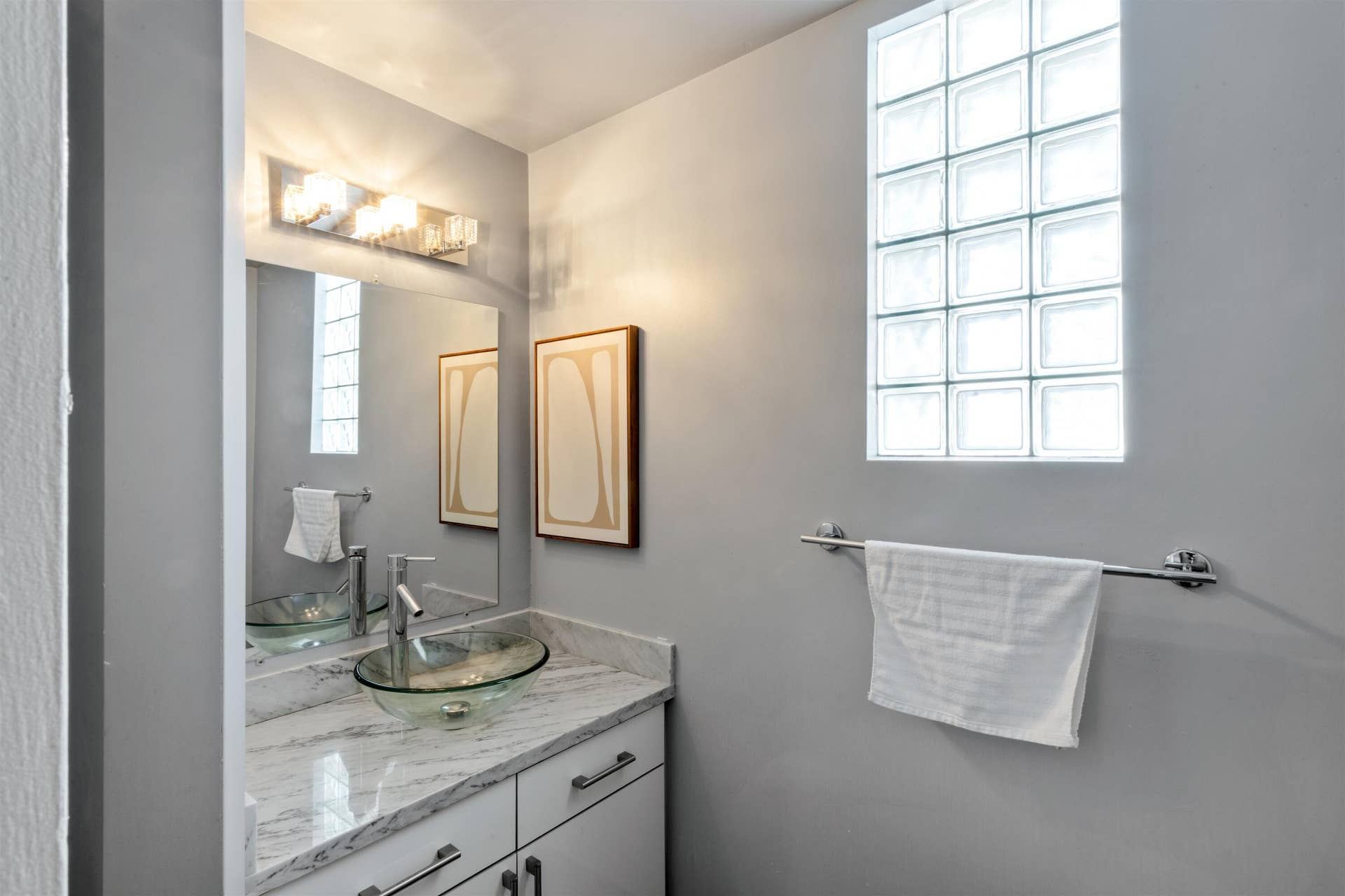 419 E Atlantic Avenue, Delray Beach, FL 33483 Stone-finish countertop featuring a glass vessel sink, modern chrome faucet, built-in cabinetry, and a glass block window