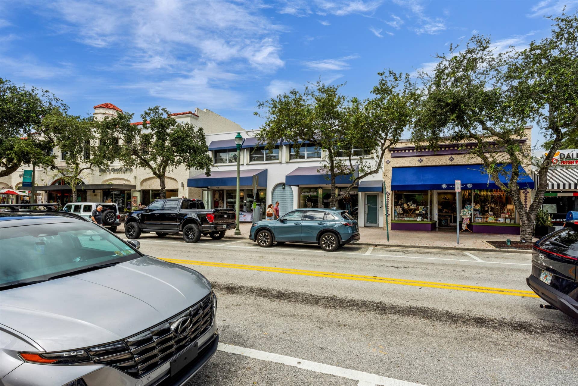 419 E Atlantic Avenue, Delray Beach, FL 33483 Commercial storefronts featuring masonry facades, multi-pane display windows, blue fabric awnings, and mature street-side trees