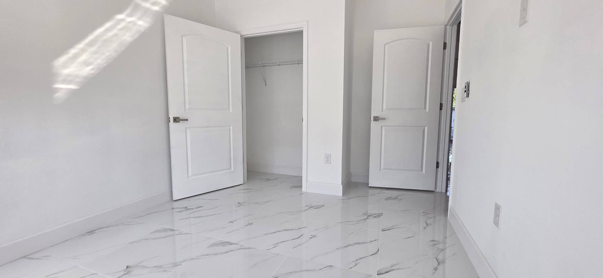Neutral-toned interior featuring large-format tile flooring with marbling detail, two-panel interior doors with satin nickel hardware, and an open closet storage area
