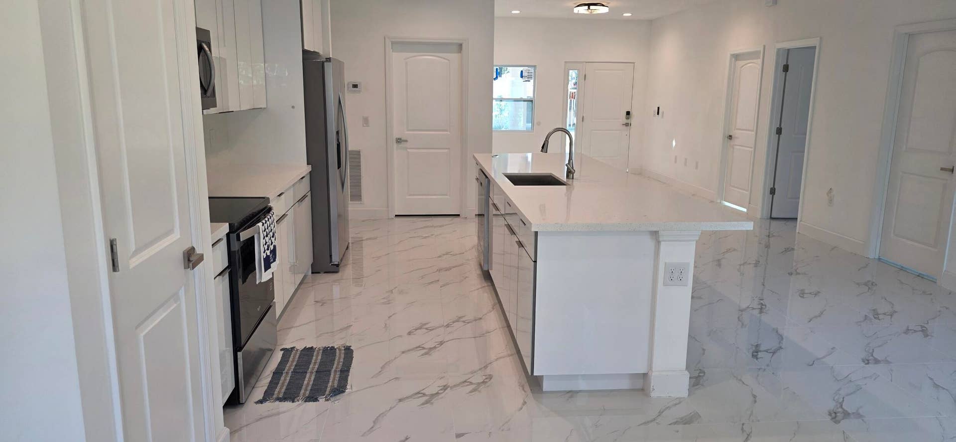 Kitchen featuring high-gloss white cabinetry, a center island with a stone-finish countertop, stainless steel appliances, and large-format tile flooring with a marble-finish pattern