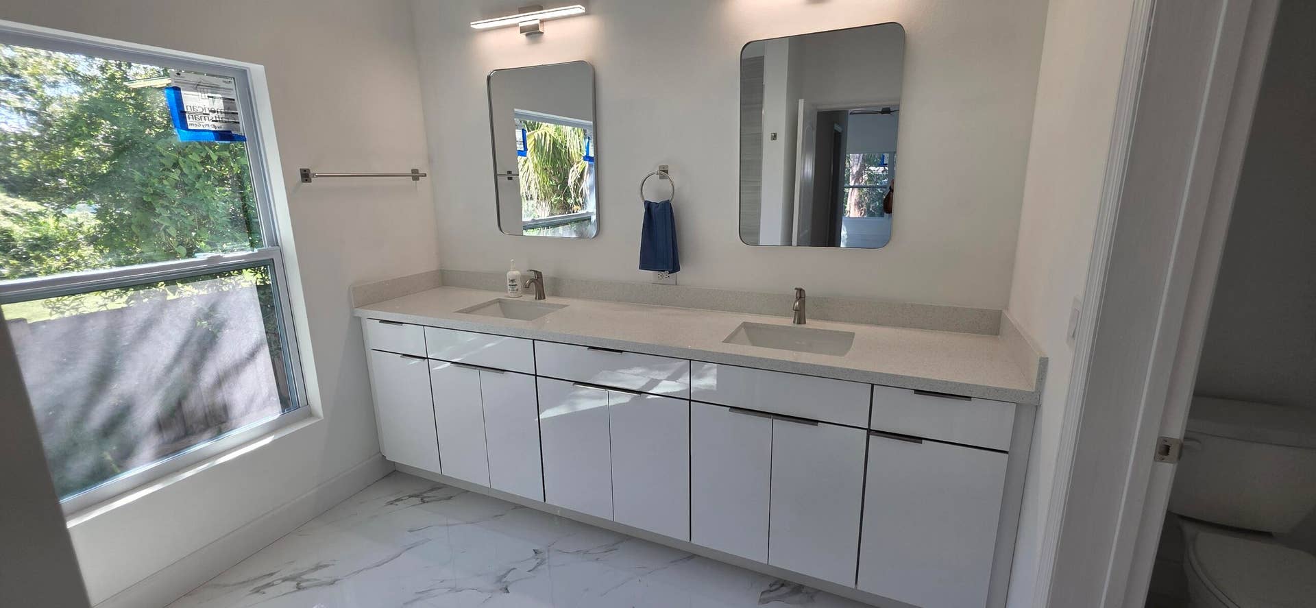 Dual-vanity cabinet with sleek white finish, expansive stone-surface countertop, dual rectangular undermount sinks, frameless wall mirrors, and high-gloss tile flooring