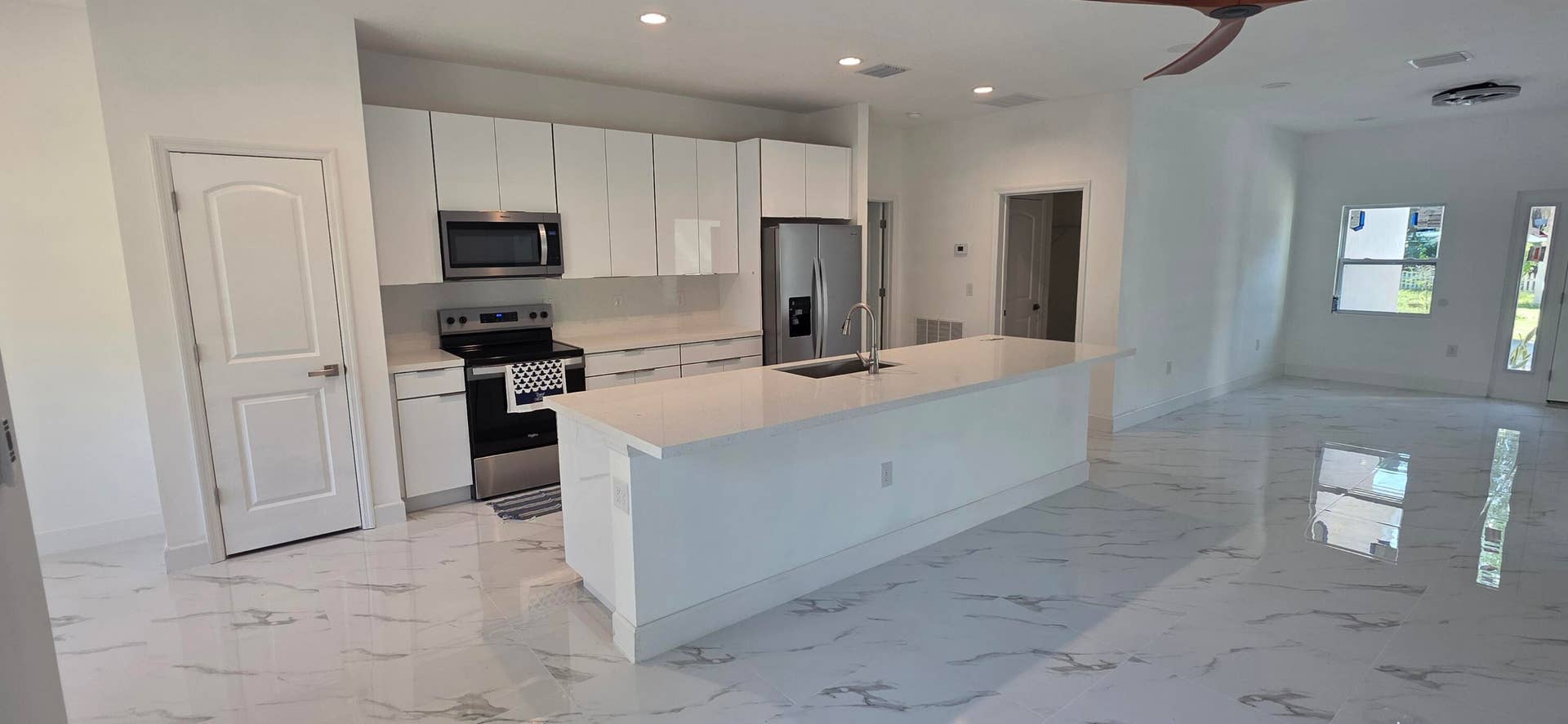 Kitchen featuring white flat-panel cabinetry, quartz countertops, a central island with an integrated sink, stainless steel appliances, and large-format tile flooring