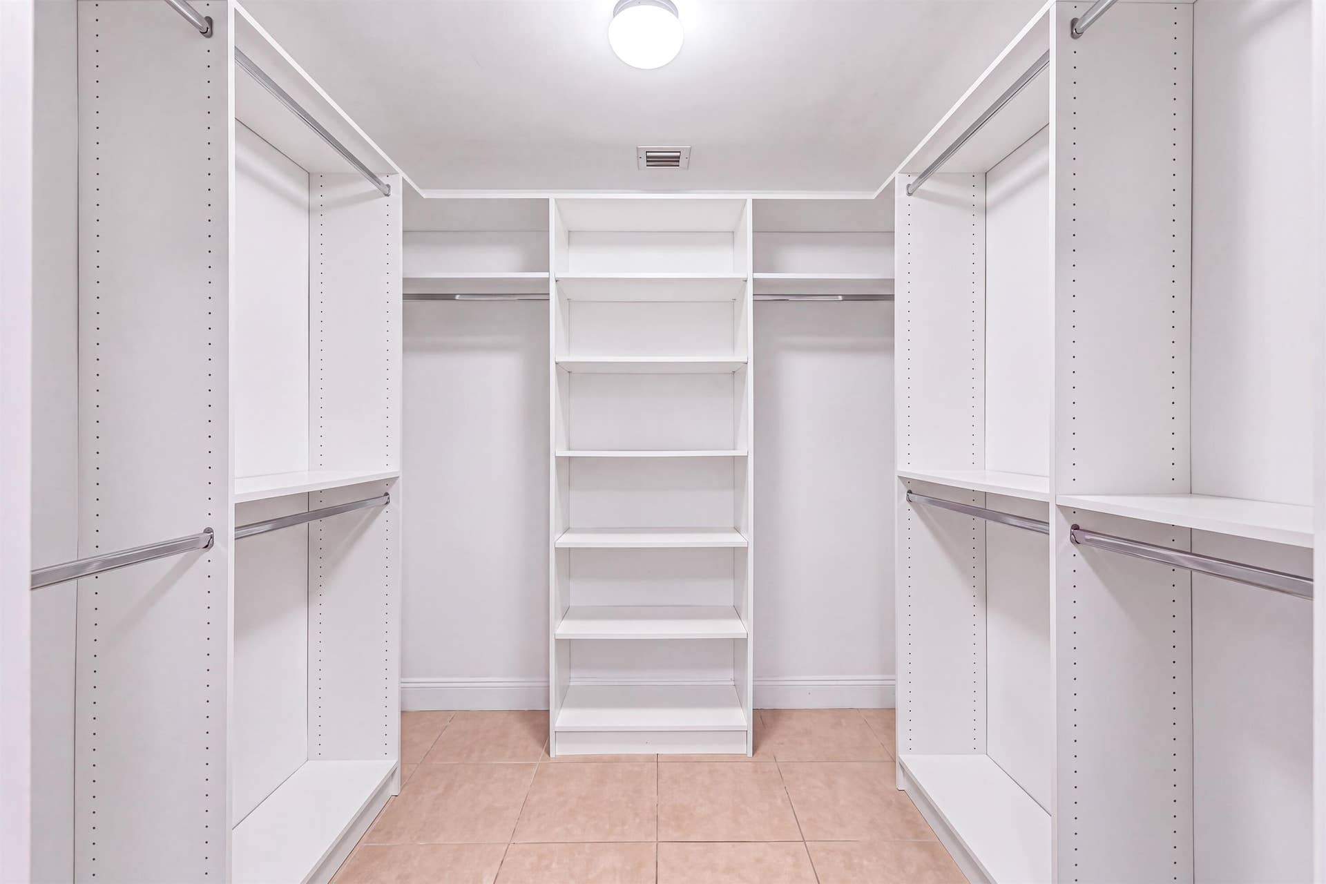 Walk-in closet featuring white built-in shelving, multiple hanging rods, and tile flooring