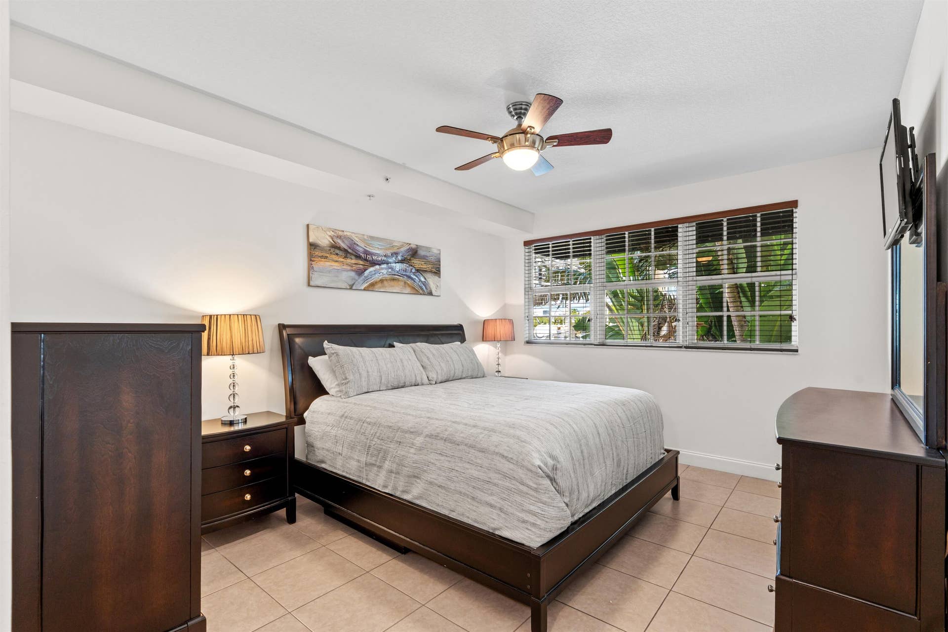 Neutral-toned interior space featuring light-colored tile flooring, oversized windows with horizontal blinds, and a ceiling fan with integrated lighting