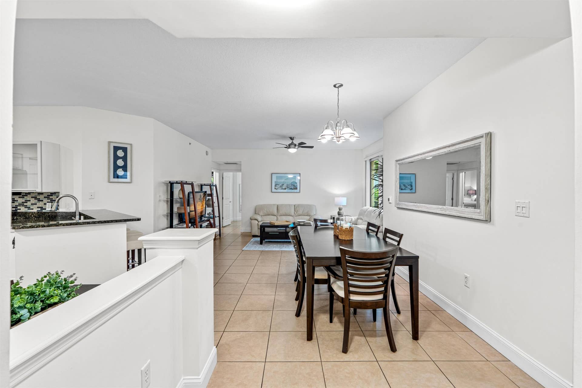 Open floor plan featuring neutral tile flooring, kitchen peninsula with a dark stone countertop, multi-light chandelier, and vaulted ceilings