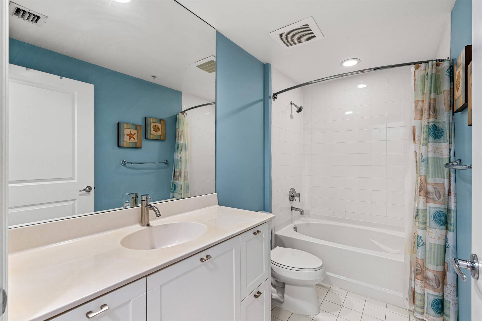 Bathroom featuring white cabinetry, integrated sink, large wall-to-wall mirror, and a tub-shower combination with tile surround