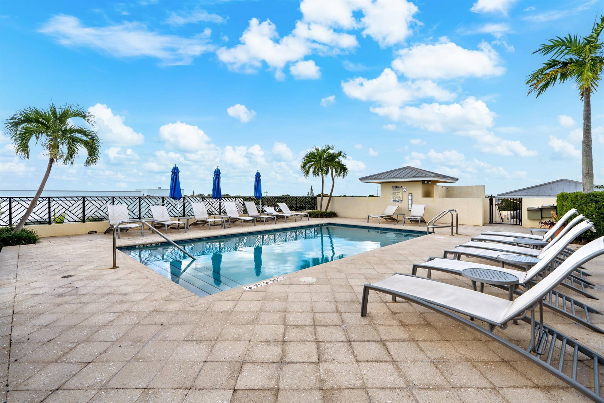 Outdoor swimming pool featuring a geometric tiled deck, metal perimeter fencing, and a covered pavilion