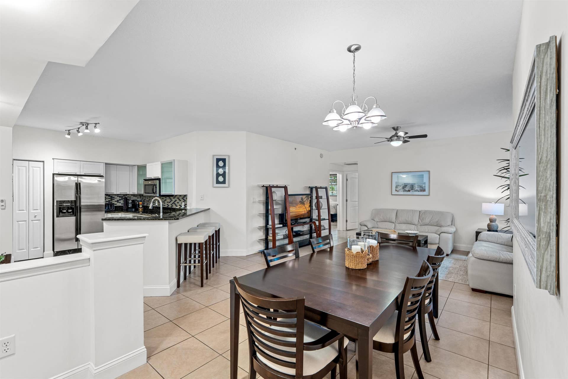 Open-concept area featuring tile flooring, a kitchen peninsula with a stone countertop, recessed lighting, and a multi-arm chandelier