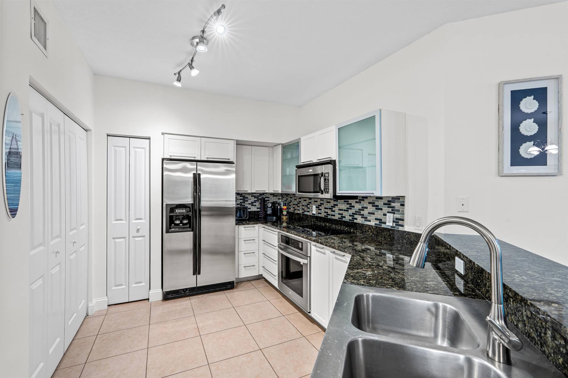 Kitchen featuring white cabinetry with glass-panel accents, dark stone countertops, stainless steel appliances, a multi-tonal mosaic tile backsplash, and ceramic floor tile