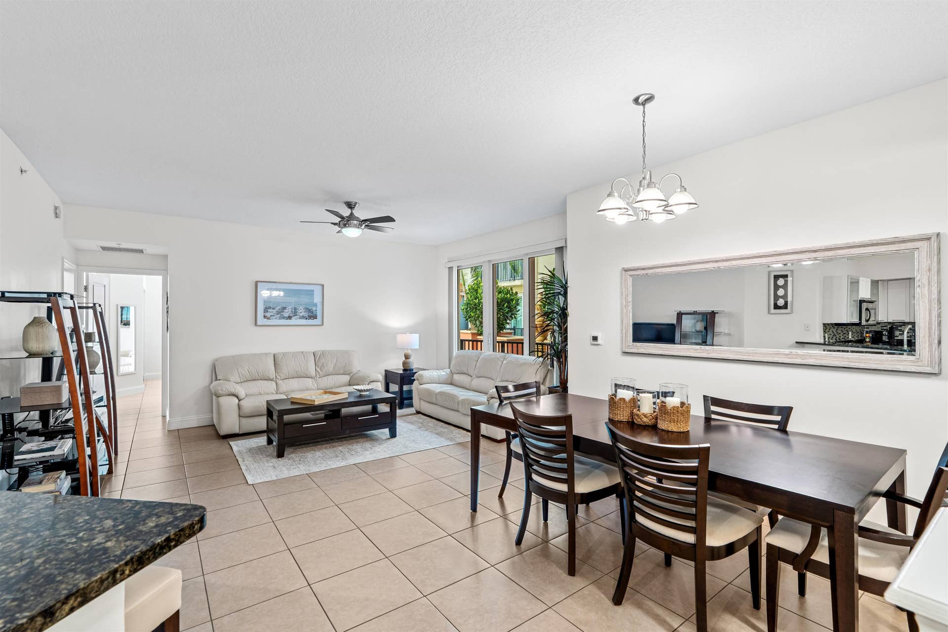 Open-concept interior featuring large-format ceramic tile flooring, a multi-arm chandelier, ceiling fan, and a wide wall-mounted mirror