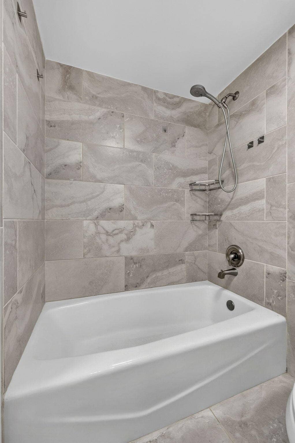 Bathtub and shower combination featuring large-format ceramic tile surround, integrated metal corner shelving, and oil-rubbed bronze plumbing fixtures