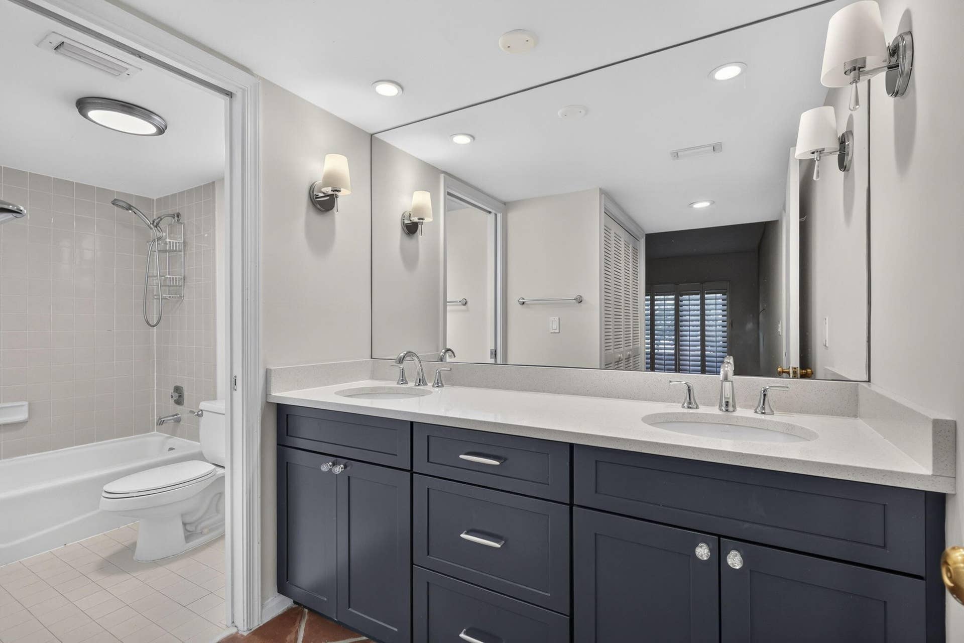 Dual-sink vanity with a solid-surface countertop, dark-toned cabinetry, recessed lighting, wall-mounted light fixtures, and a tiled shower-tub combination