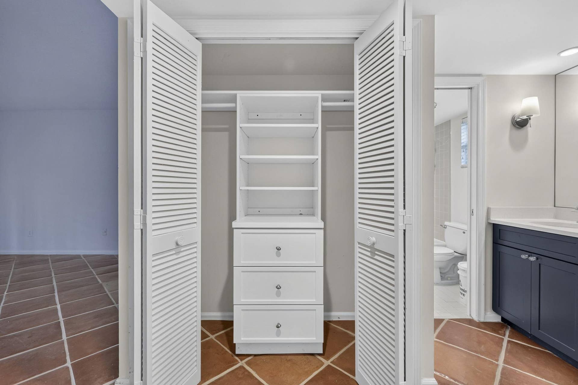 Built-in closet featuring white louvered bifold doors, integrated shelving, and three storage drawers