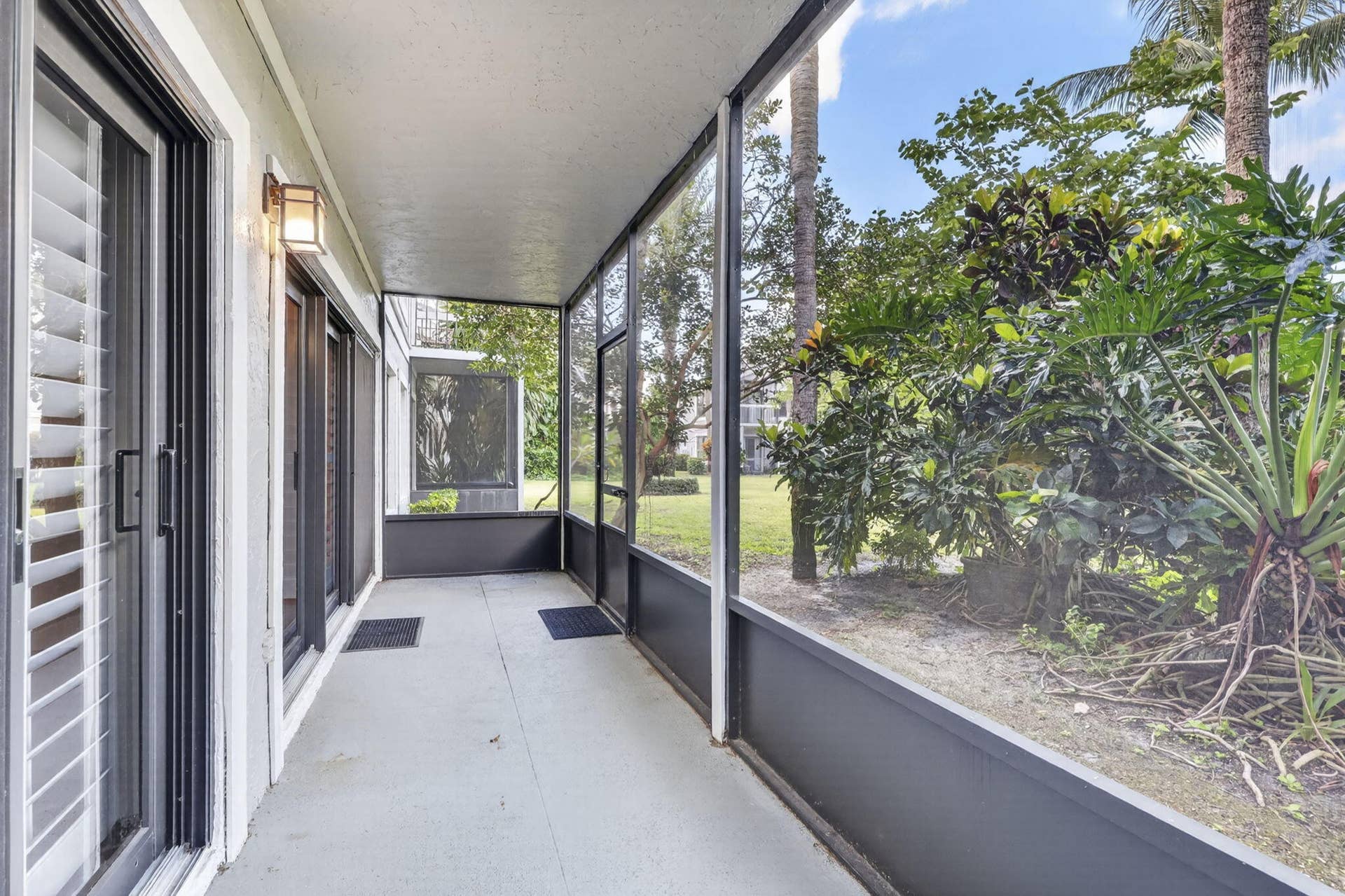 Screened-in lanai featuring concrete flooring, aluminum framing, and wall-mounted exterior lighting