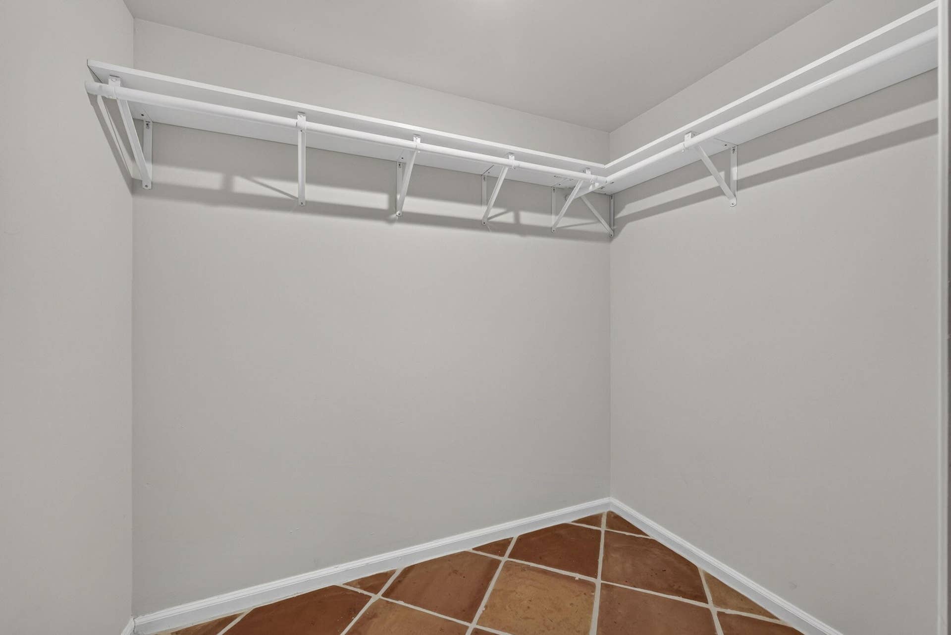 Storage area featuring neutral wall paint, white wrap-around shelving, and terracotta-tone tile flooring laid in a diagonal pattern