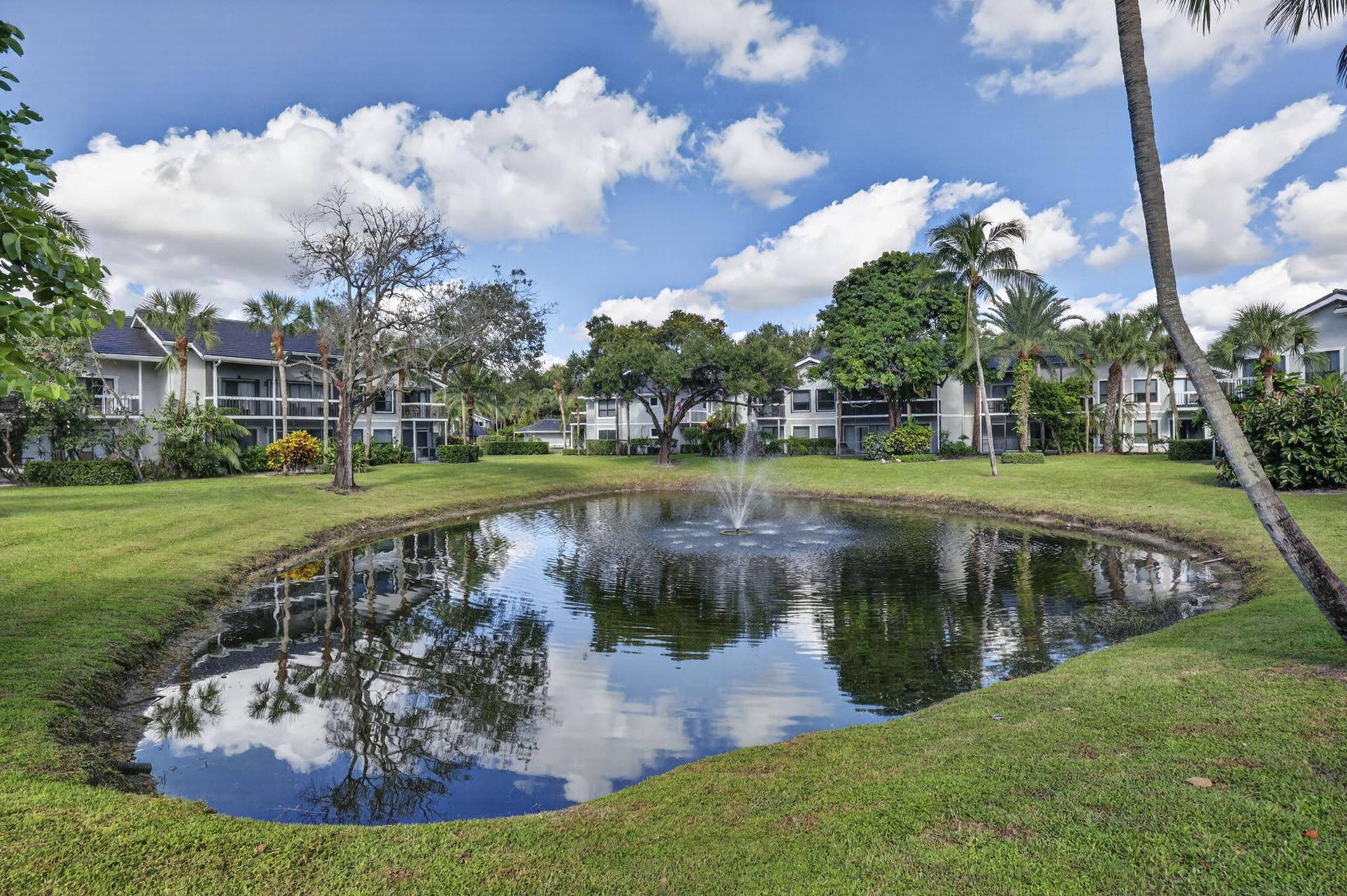 Landscaped grounds featuring a central pond with a fountain, mature palm trees, and expansive lawn areas