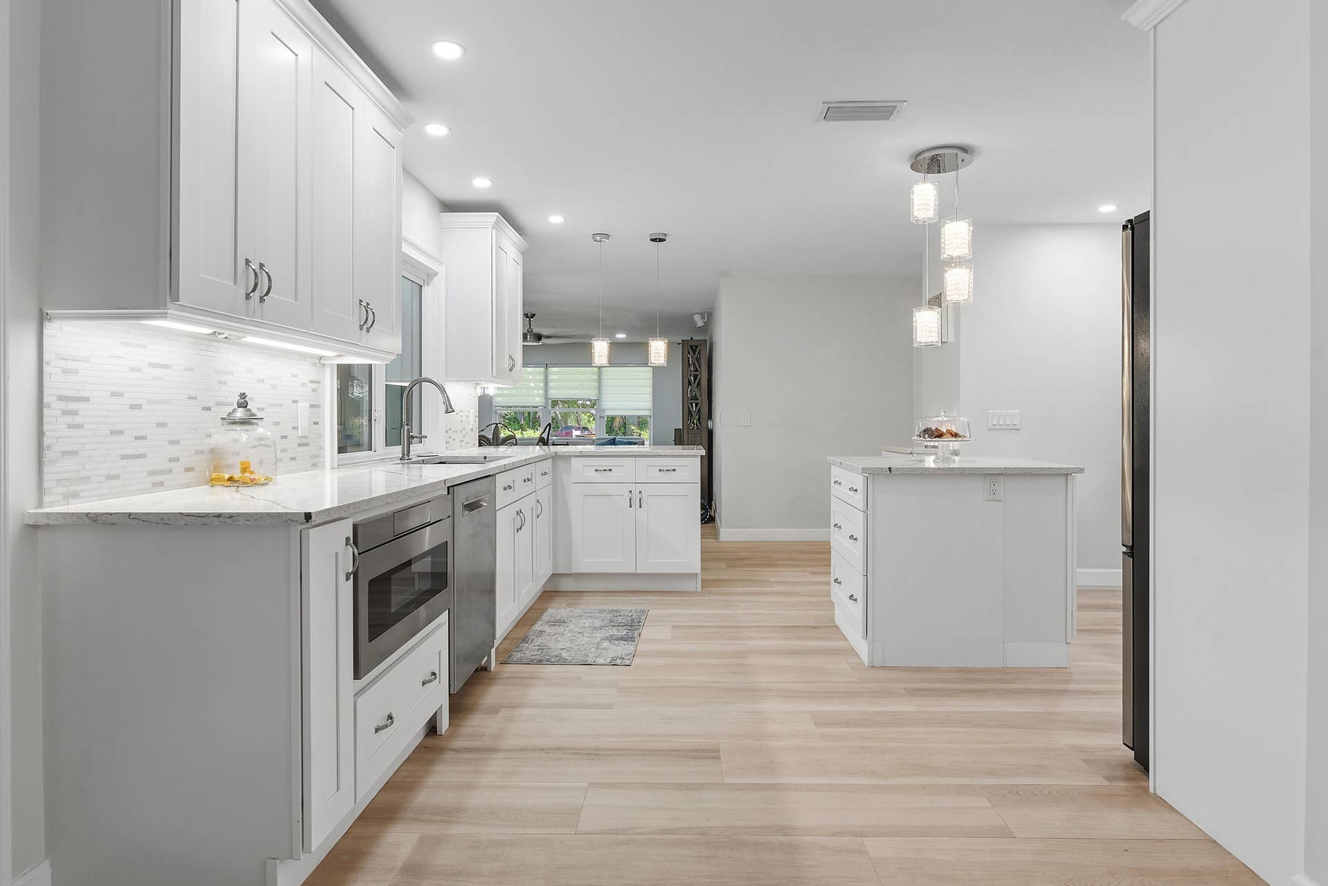 3098 SE BUR Street, Port St Lucie, FL 34952 beautifully remodeled kitchen featuring abundant white cabinetry, marble-look countertops, stainless steel appliances, stylish pendant lighting, and a spacious prep island. A chef's dream!