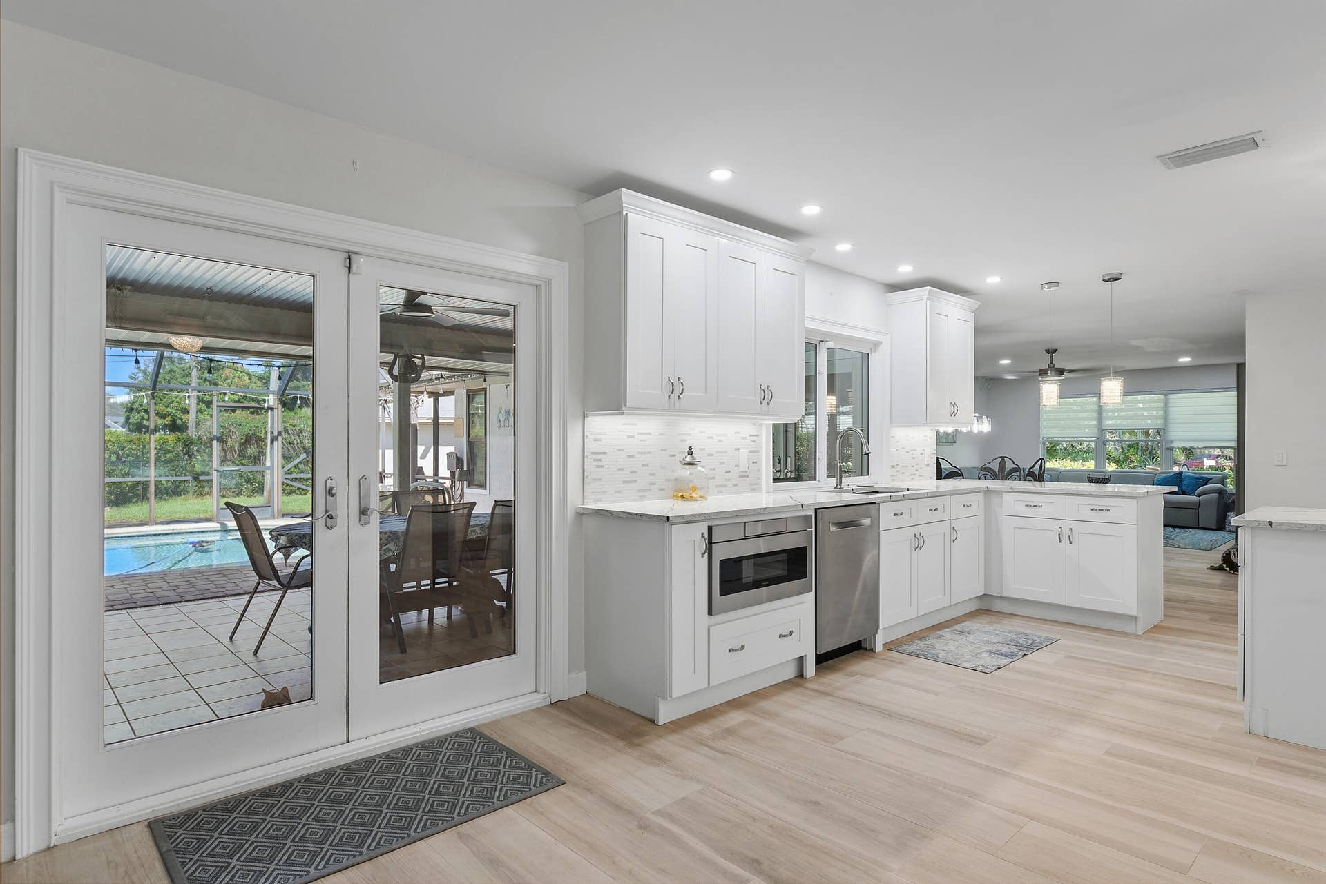 3098 SE BUR Street, Port St Lucie, FL 34952 Beautifully remodeled kitchen with white cabinetry, marble-look countertops, and French doors leading to the spacious screened lanai and pool. Perfect for indoor-outdoor entertaining!